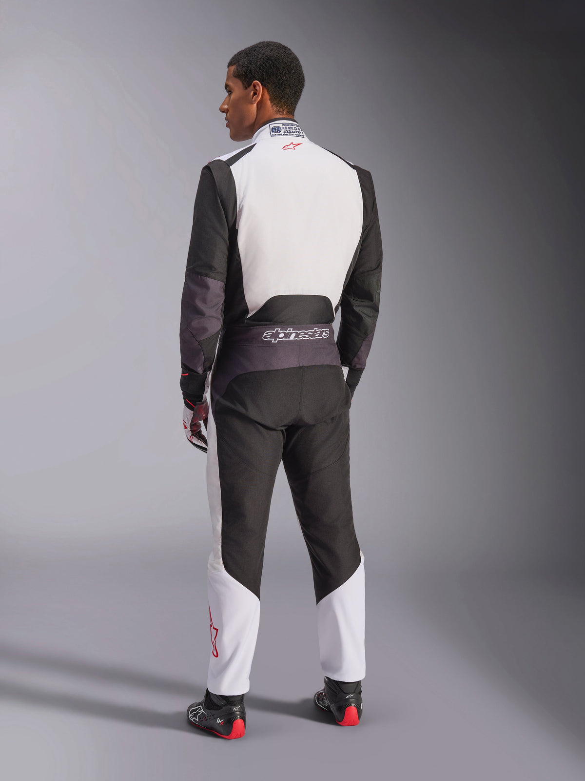 Alpinestars KMX-5 V3 Suit, Karting Suit, White Black and Bright Red, rear view of a man wearing a one-piece racing suit with a white upper back and black lower panels, featuring a small red logo on the collar, worn with professional racing boots and gloves