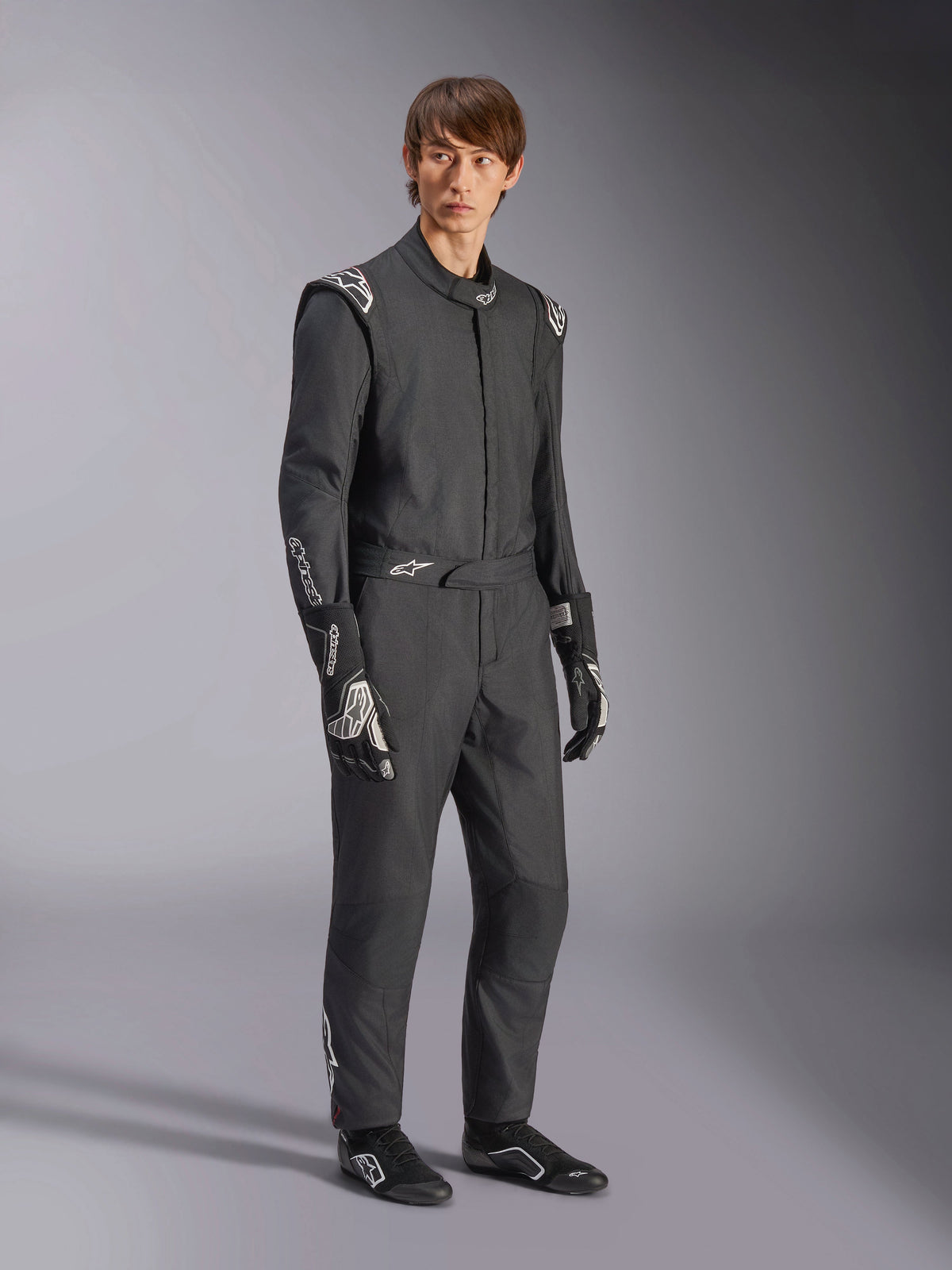 Mono Alpinestars GP Tech V4, traje de automovilismo de una pieza, negro y blanco, usado con guantes y calzado de carreras a juego, con logotipos blancos en los hombros y antebrazos, diseño profesional elegante para automovilismo