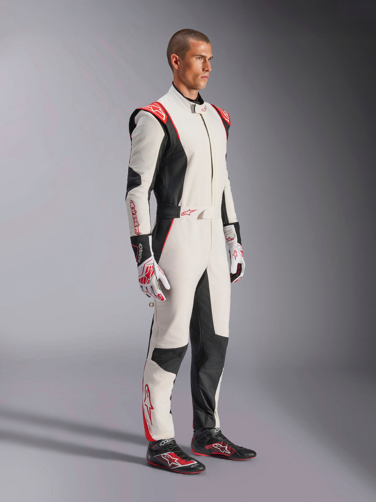 Piloto de carreras masculino con el mono Alpinestars GP Tech V4 en blanco, negro y rojo, traje de automovilismo de una sola pieza, guantes y calzado de competición a juego, equipamiento profesional de automovilismo con marca Alpinestars y diseño ergonómico