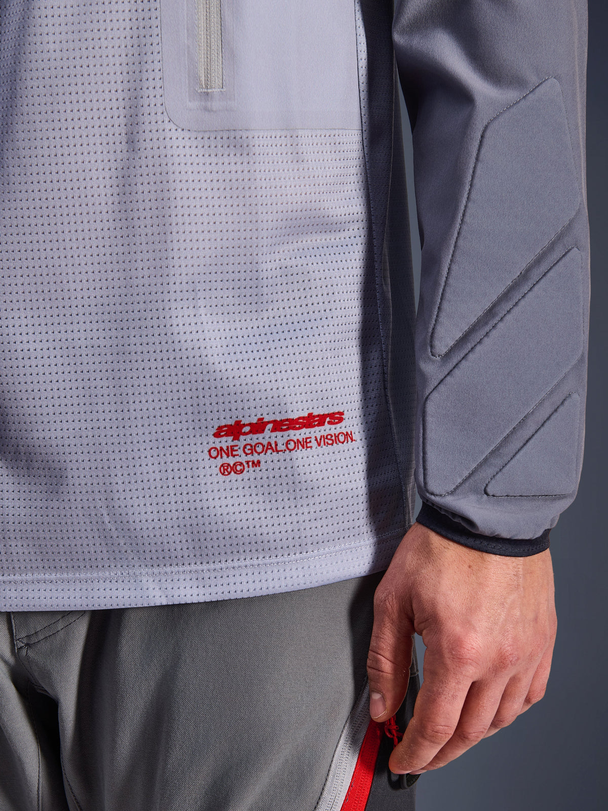 Alpinestars Maxdura Dual Jersey, Mid Gray and Dark Gray, close-up showing breathable mesh torso with red branding, zippered pocket detail, and integrated padding on the sleeve, technical adventure motorcycle gear