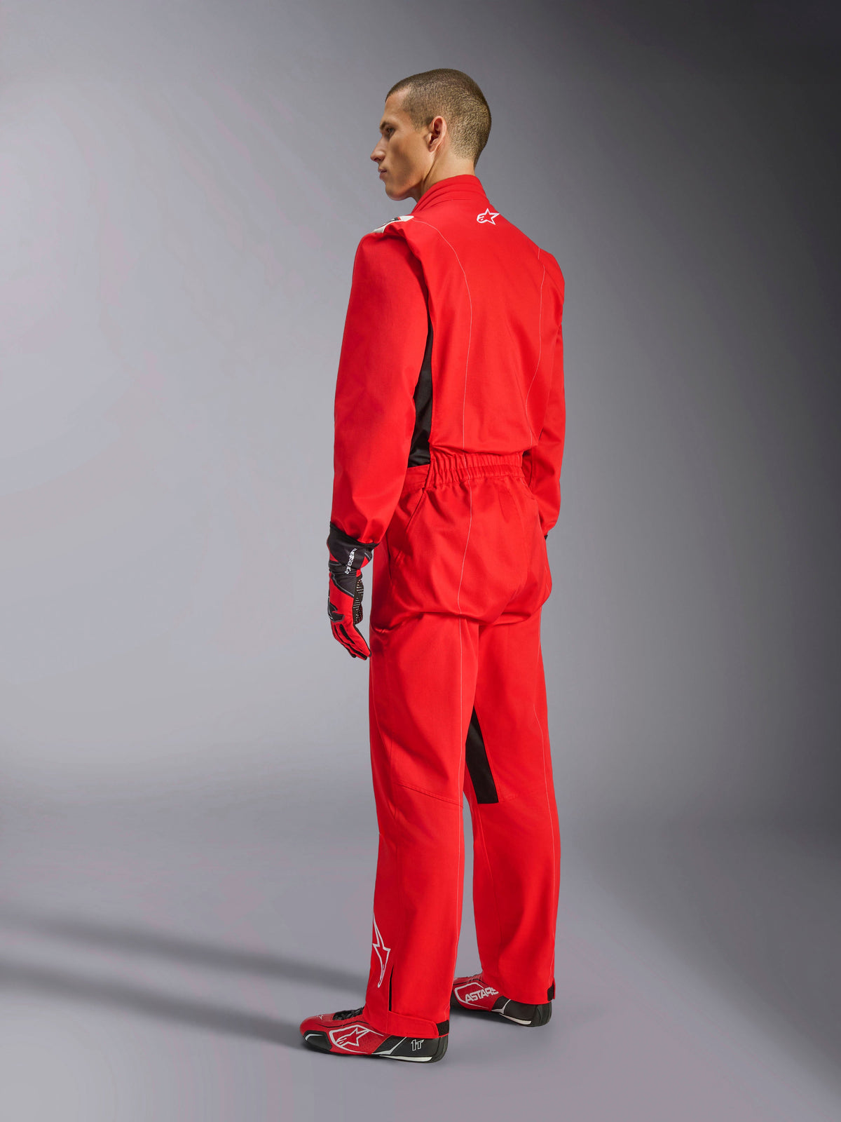 Alpinestars Kart Indoor V2 Suit, Red karting suit, rear three-quarter view on a model, worn with matching red gloves and racing shoes, single-layer poly-cotton twill construction, professional motorsport gear for indoor karting.