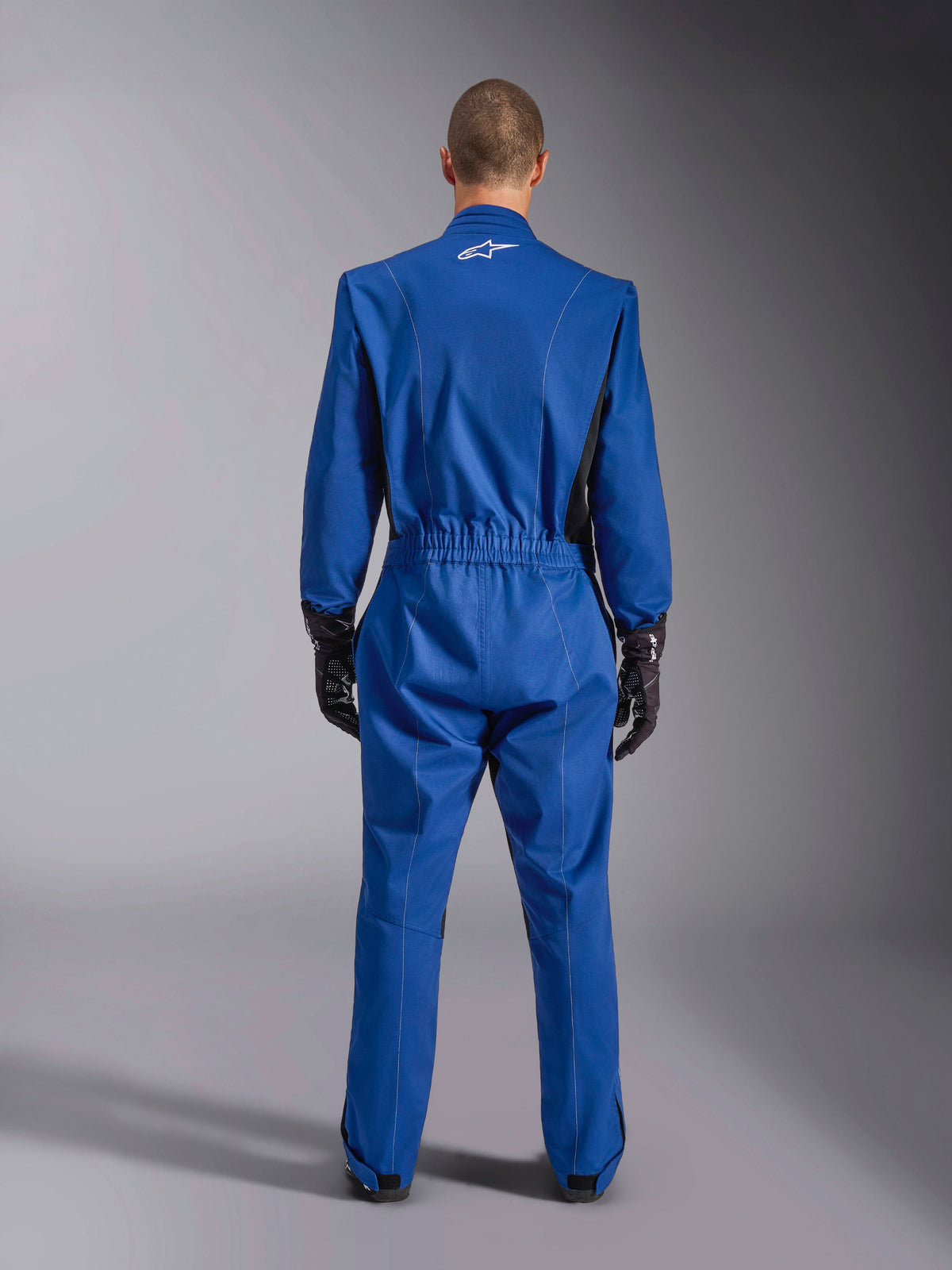 Alpinestars Kart Indoor V2 Suit, Blue, Back View, one-piece karting suit featuring a white logo on the upper back, elasticated waist, and black accents, worn with black racing gloves