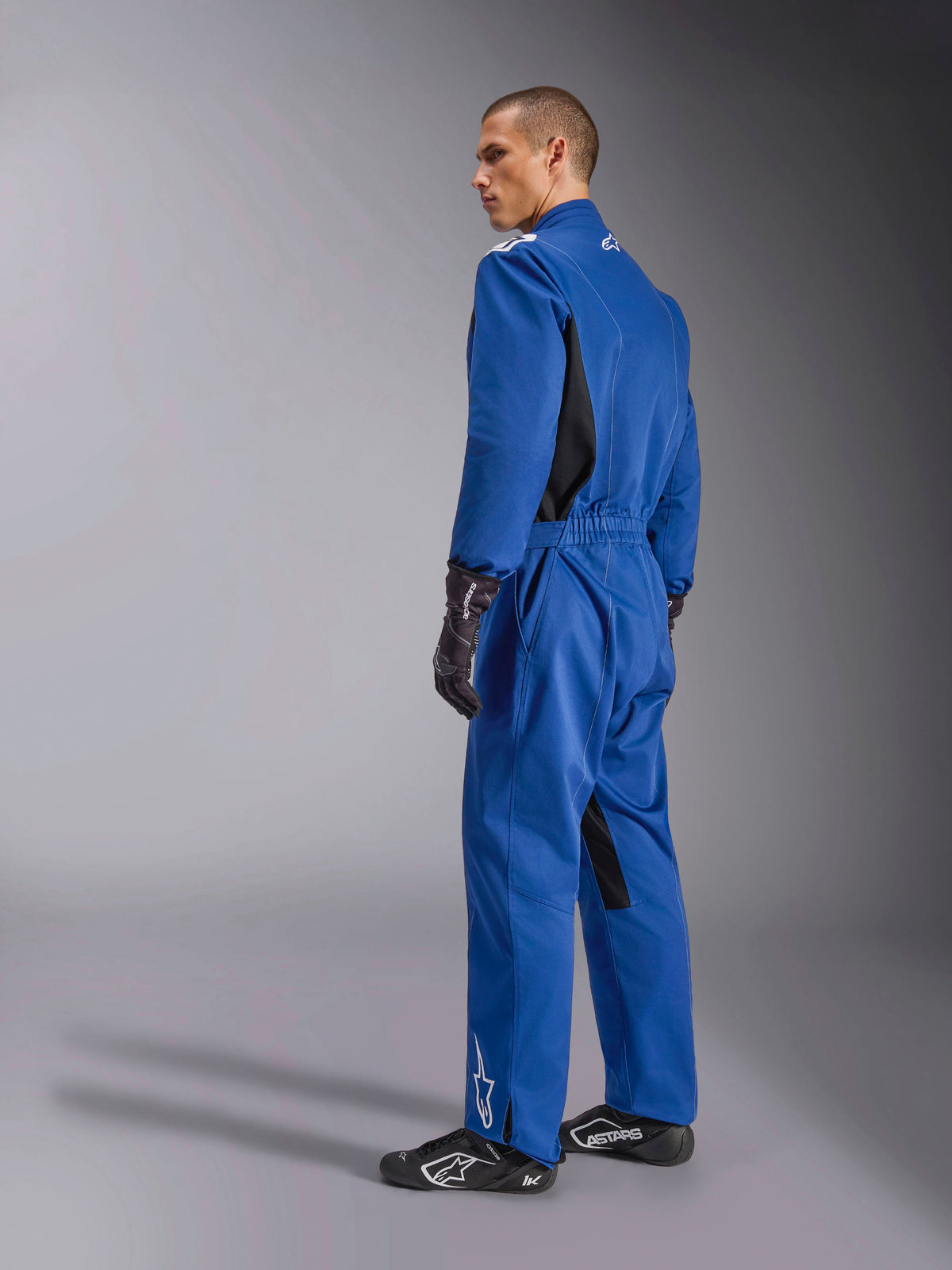 Alpinestars Kart Indoor V2 Suit, Blue karting suit, back and side view, one-piece racing suit with black side panels and inner leg accents, elastic waist and white logos, worn with black racing gloves and footwear