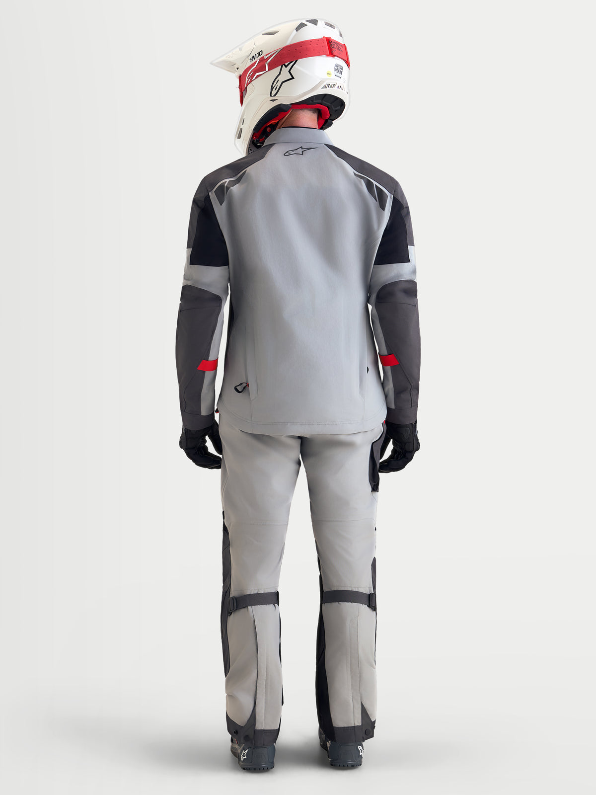 Alpinestars Arenis Gore-Tex Chaqueta, chaqueta de moto de aventura para hombre en gris medio, gris oscuro y negro, vista trasera de un modelo que lleva la chaqueta textil impermeable con casco y equipamiento de moto