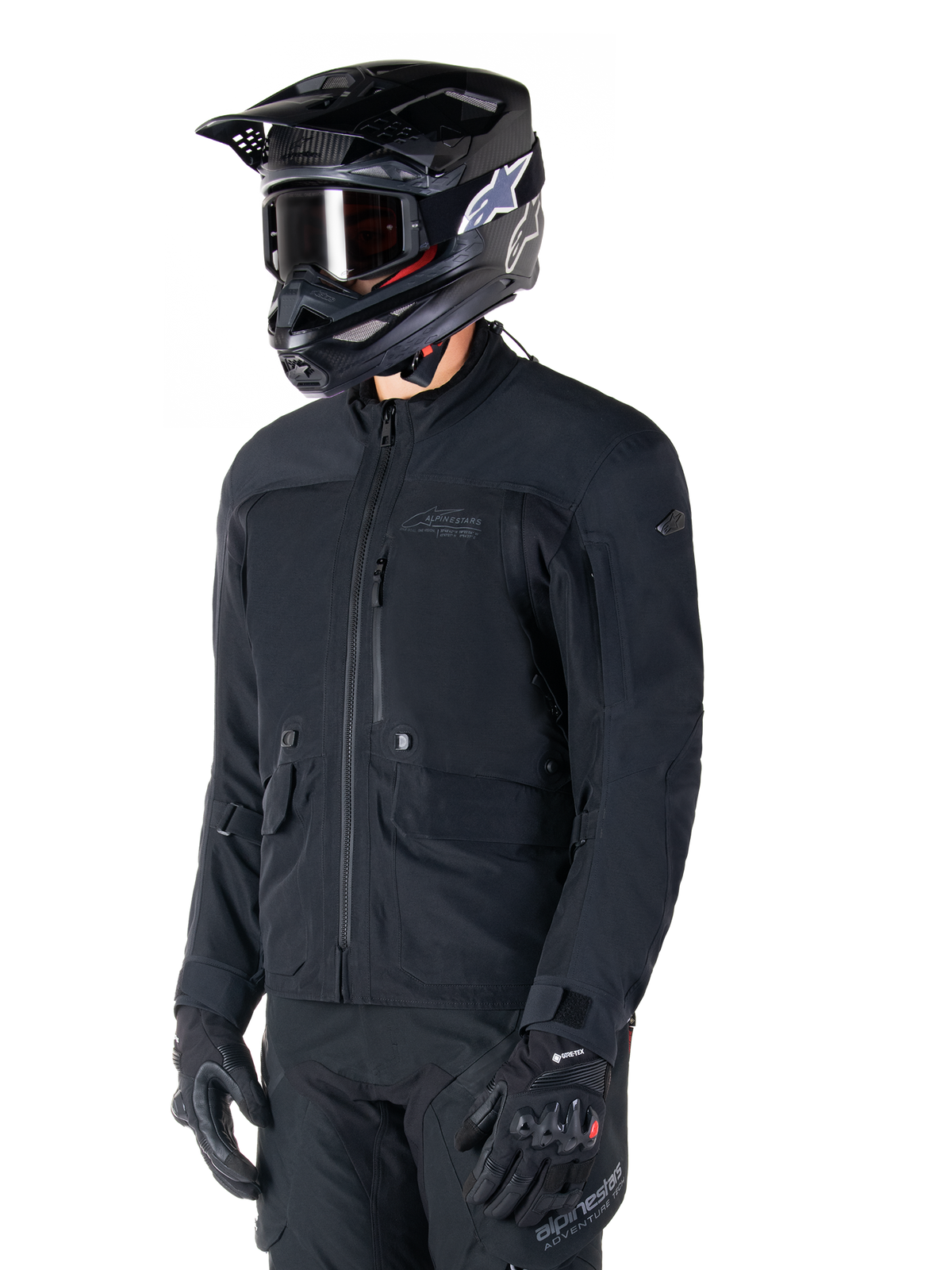 Chaqueta Alpinestars St-7 Prime GORE-TEX, chaqueta de moto negra, usada por un piloto con casco negro y gafas, con grandes bolsillos de carga en el pecho y capa exterior laminada impermeable, equipamiento premium para touring de aventura y desplazamientos diarios