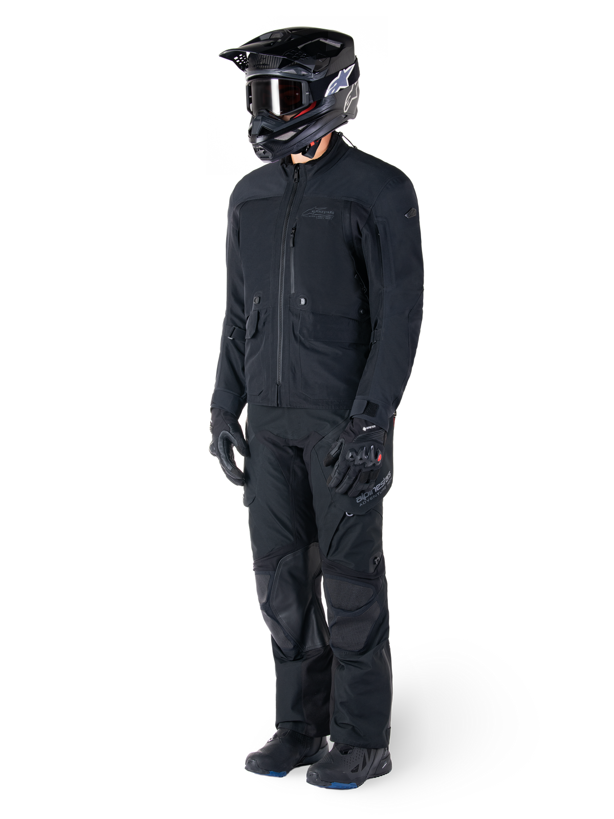 Motociclista con la chaqueta Alpinestars St-7 Prime GORE-TEX en color negro, conjunto de aventura coordinado con pantalones negros a juego, casco negro con gafas y guantes, con un diseño aerodinámico y funcional para un rendimiento óptimo en cualquier condición climática.