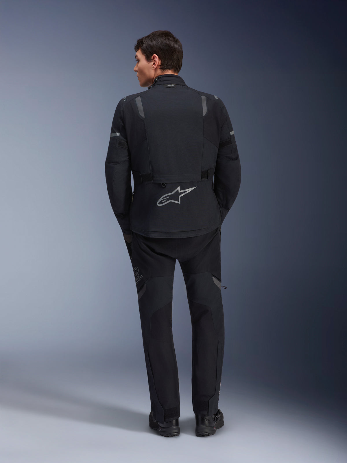 Alpinestars ST-7 2L GORE-TEX Jacket and matching ST-7 2L GORE-TEX Pants, Black and Dark Gray adventure motorcycle gear, rear view showing reflective Alpinestars logo on the jacket and technical textile construction.
