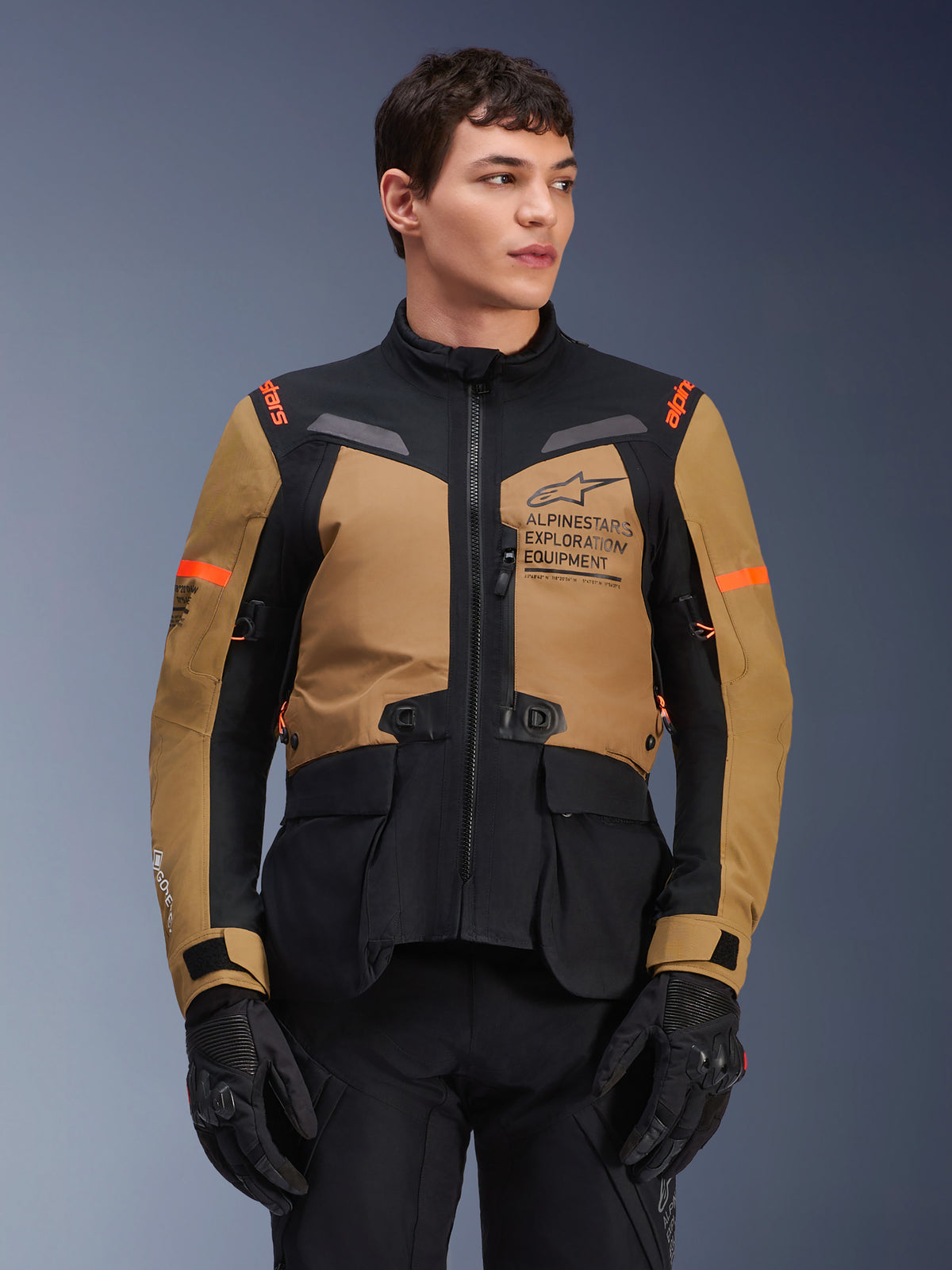 Alpinestars ST-7 2L GORE-TEX Jacket, Motorcycle Adventure Touring Jacket, Gobi Brown and Black with orange accents, worn by a male model, featuring Exploration Equipment branding and GORE-TEX technology, durable waterproof riding gear.