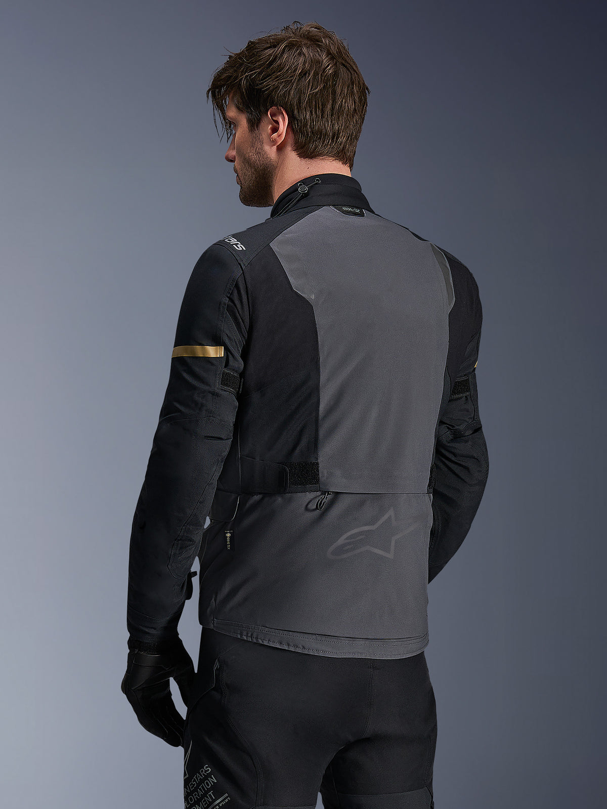 Chaqueta Alpinestars ST-7 2L GORE-TEX, chaqueta de moto, gris oscuro, negro y caqui oscuro, vista trasera que muestra un gran panel posterior gris con marca sutil, mangas negras con detalles en caqui de tono dorado, diseño textil impermeable preparado para la aventura