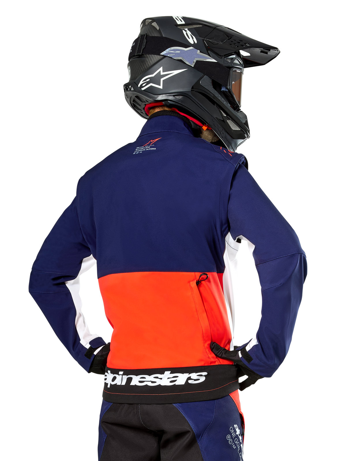 Alpinestars Lite-Dura Softshell Jacket, Navy Hot Orange and White, rear view worn by a motocross rider, featuring a large white logo on the back hem and zippered storage pocket, part of a complete off-road racing outfit.