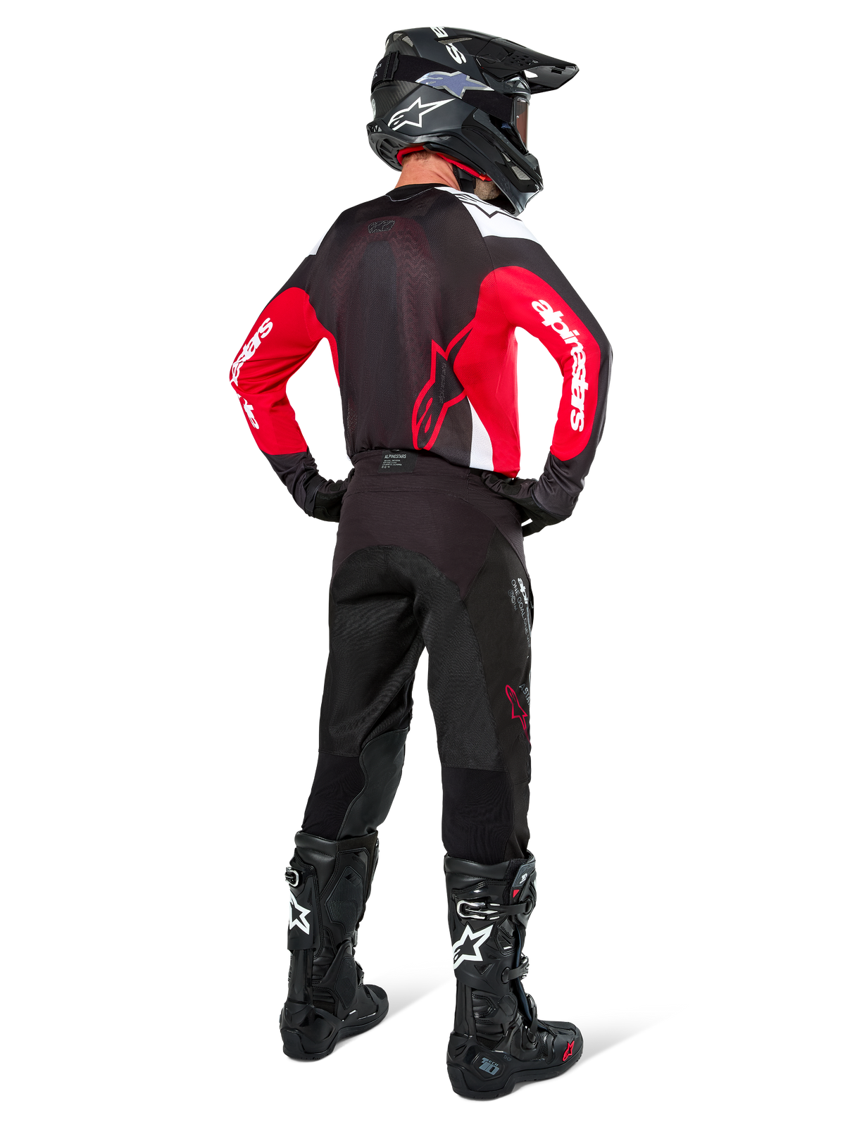 Piloto de motocross visto desde atrás vistiendo pantalones Alpinestars Pro-Dura en color Black Magnet White, combinados con un jersey rojo y negro y botas negras, conjunto coordinado de equipamiento off-road para enduro