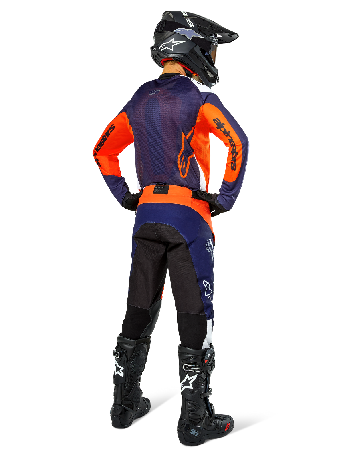 Piloto de motocross con equipamiento completo de carreras visto desde atrás, jersey azul navy y naranja, pantalones Pro-Dura en Navy Hot Orange White, casco negro y botas negras, conjunto profesional de competición off-road.