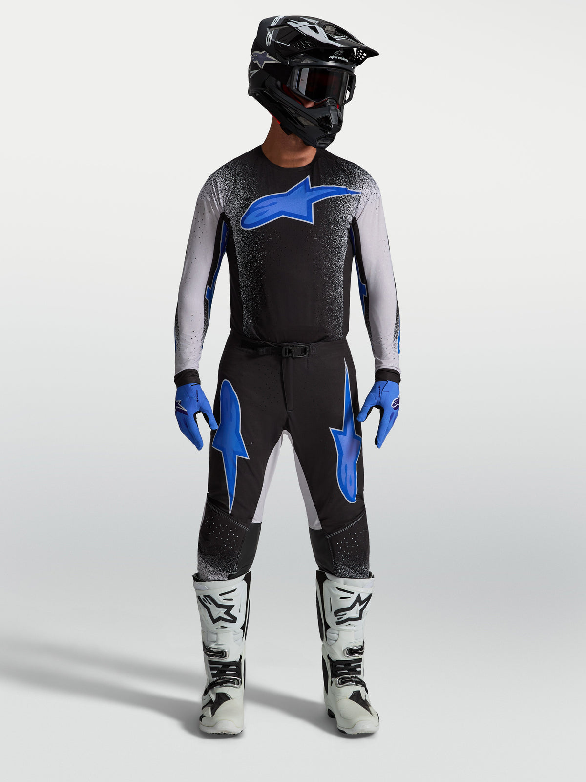 Pantalones Alpinestars Supertech Hiten AFD, equipo de motocross negro y azul, con jersey a juego y botas de carreras blancas.