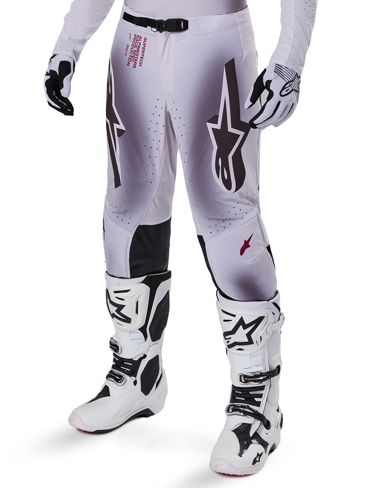 Pantalones Alpinestars Supertech Maker 2025, pantalones de motocross, en color plata y negro, con logotipos de estrellas grandes y letras rojas, mostrados con botas y guantes blancos a juego