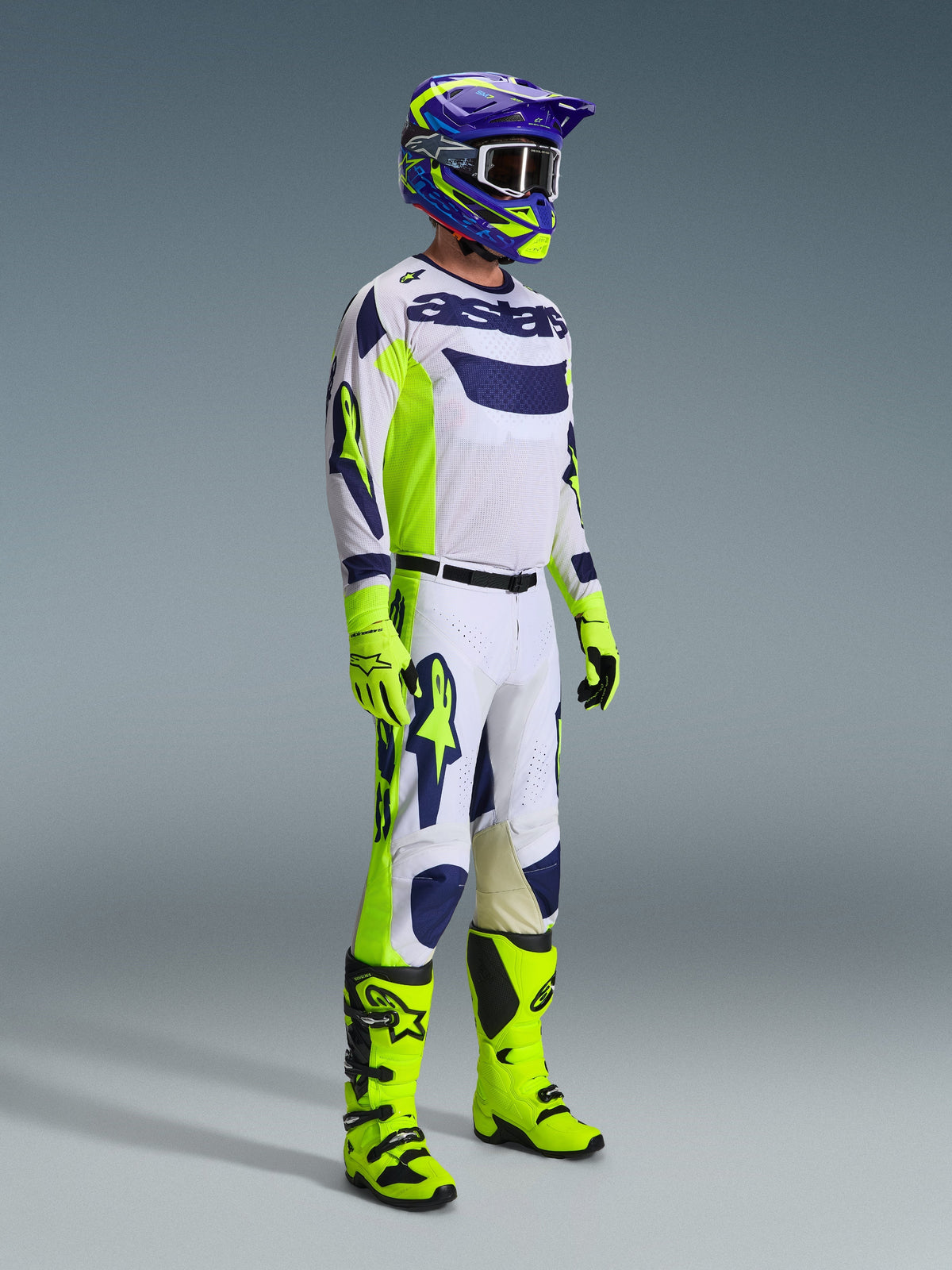 Motocross rider wearing complete racing gear, 2026 Racer Air Riway Pants in Light Gray Yellow Fluo Blue, matching white and blue jersey, fluo yellow gloves and boots, and a blue and yellow helmet, coordinated outfit for professional off-road performance