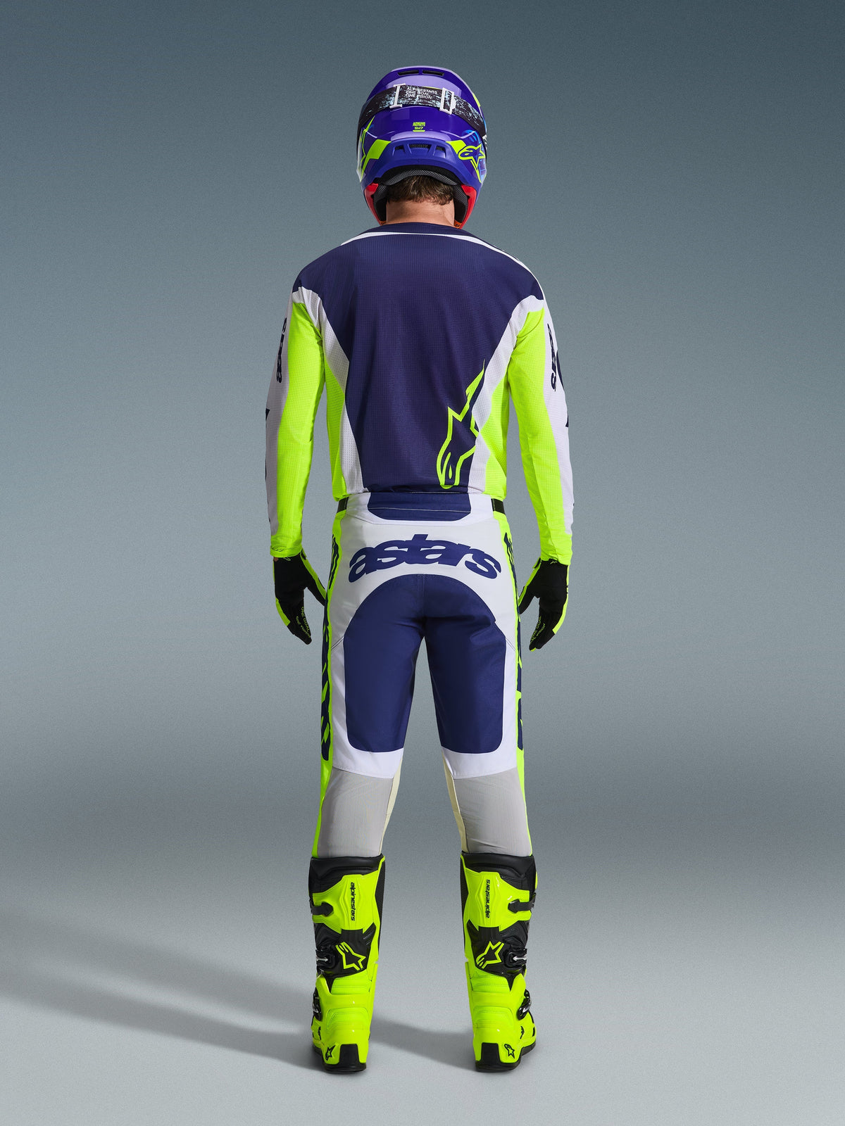 Motocross rider from the back wearing the Alpinestars 2026 Racer Air Riway Pants in Light Gray, Yellow Fluo, and Blue, paired with a matching jersey and bright yellow boots, illustrating a complete professional off-road racing gear set.