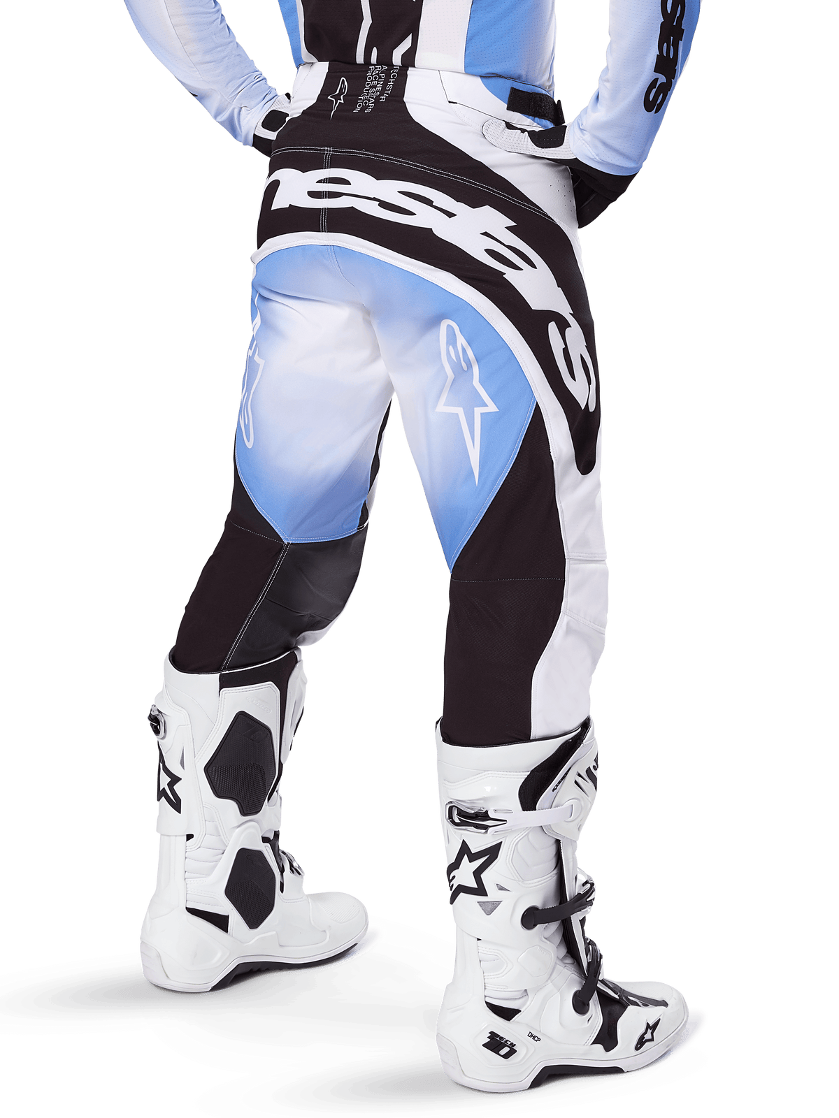 Alpinestars Techstar Melt Pants 2025, pantalones de motocross, negro, azul y blanco, vista posterior con el nombre de la marca Alpinestars destacado en el asiento y logotipos de estrella en las piernas, combinados con botas Tech 10 blancas y negras, equipo profesional de carreras todoterreno