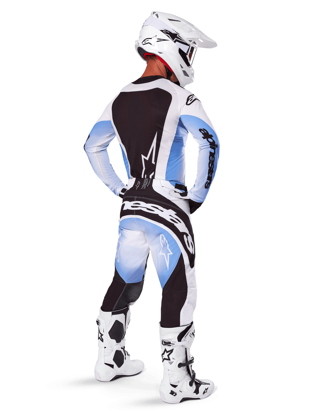 Alpinestars 2025 Techstar Melt, piloto de motocross visto desde atrás vistiendo jersey y pantalones con diseño degradado en negro, azul y blanco, casco blanco, botas blancas y negras, equipamiento completo de competición todoterreno