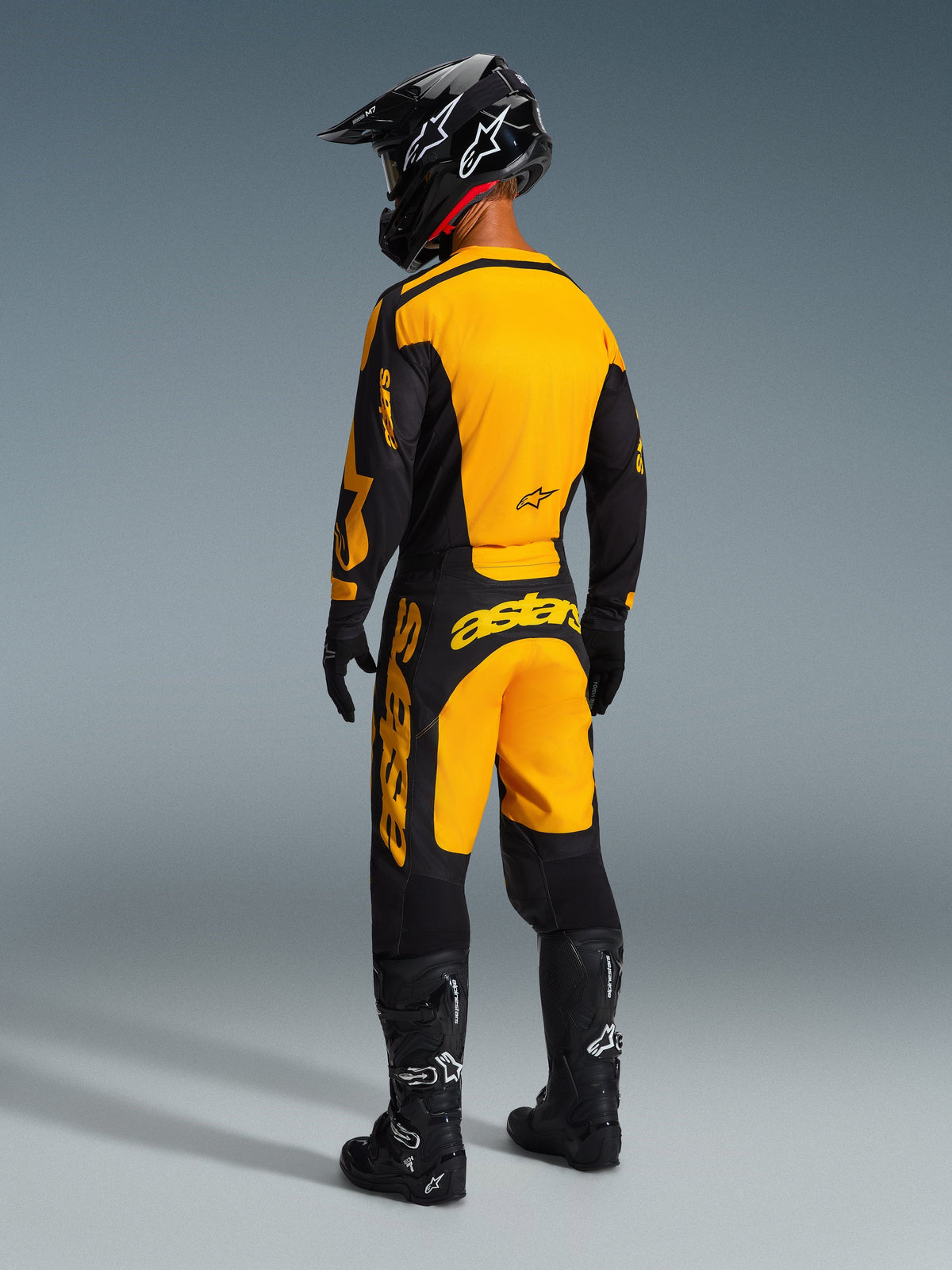 Rear view of a motocross rider wearing the Alpinestars 2026 Racer Riway Pants in Yellow and Black, matching jersey, black helmet, and black boots, coordinated racing gear set for off-road performance