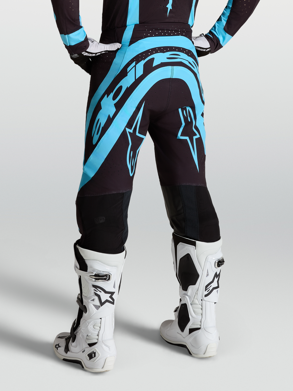Alpinestars Supertech Vesta, pantalones de motocross para hombre, negros y turquesas, vista trasera con botas blancas