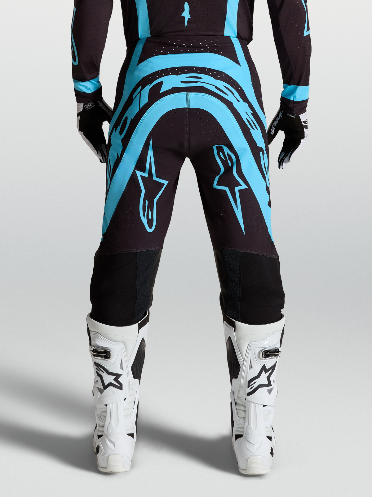Alpinestars Supertech Vesta, pantalones de motocross para carreras, negros y turquesas, con botas off-road blancas.