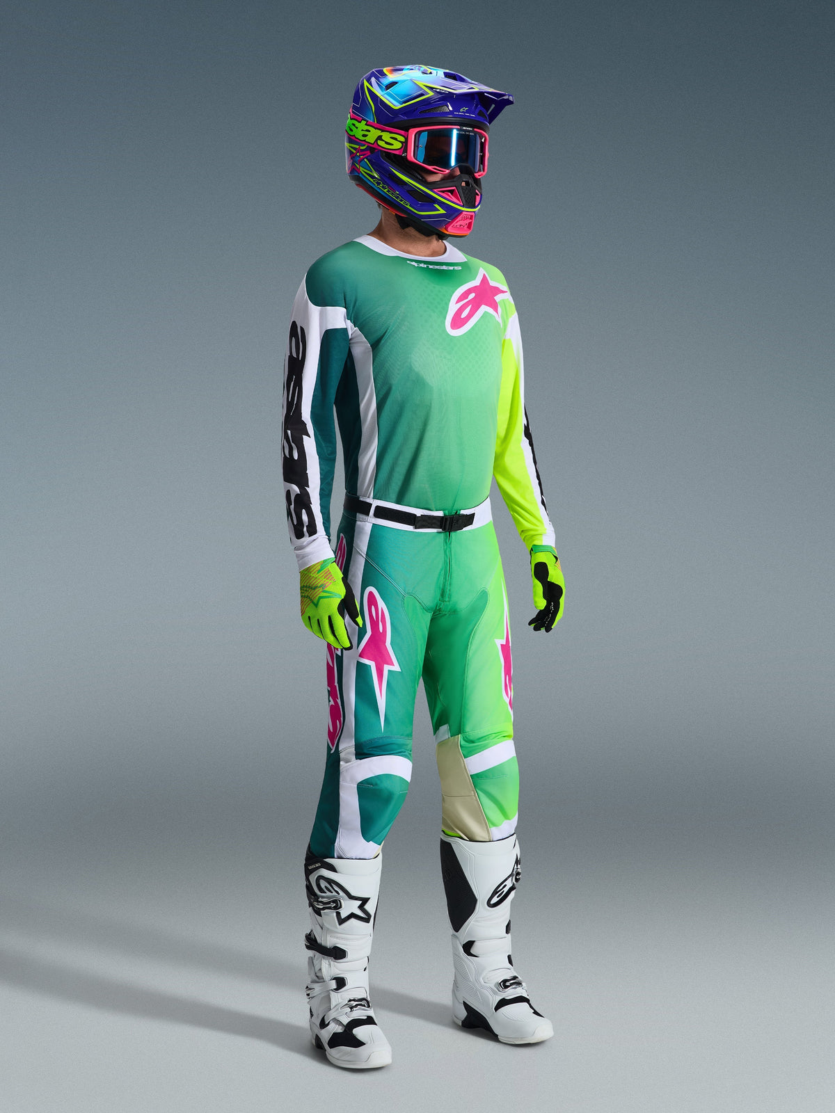Piloto de motocross con pantalones Alpinestars 2026 Racer Portl y jersey a juego en verde, blanco y negro con detalles de logotipos en rosa, casco colorido, botas de carrera blancas y negras, y guantes verde neón, conjunto completo de equipo para carreras todoterreno