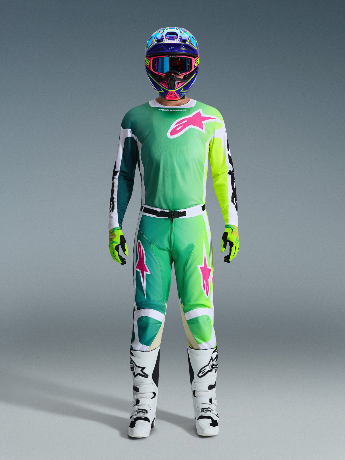 Alpinestars 2026 Racer Portl Pants, pantalones de motocross, verdes, blancos y negros con detalles de logo en rosa, usados como parte de un conjunto completo de equipamiento de carreras con jersey a juego, botas blancas y casco multicolor, atuendo coordinado para competición profesional todoterreno.