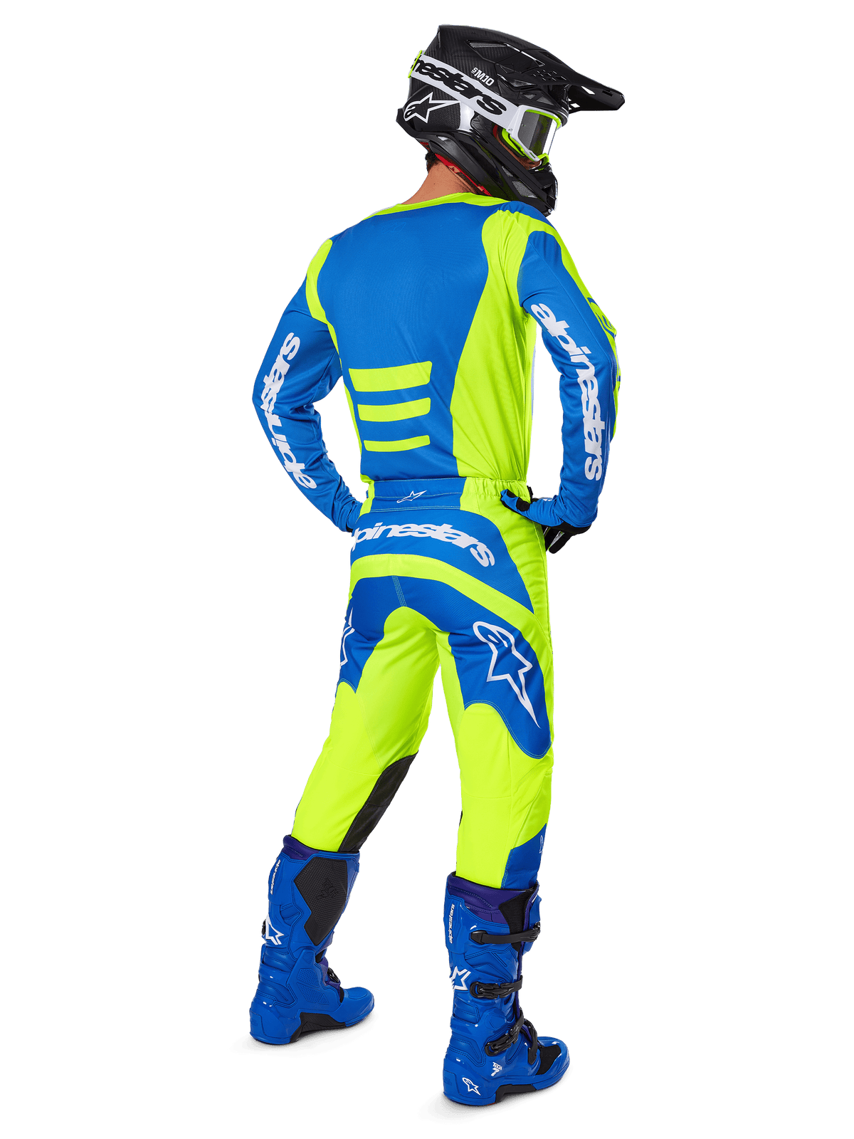 Piloto de motocross visto desde atrás vistiendo los pantalones Alpinestars 2025 Fluid Haul y el jersey a juego en amarillo flúor y azul, coordinado con botas azules y un casco Alpinestars negro, equipamiento profesional de carreras todoterreno