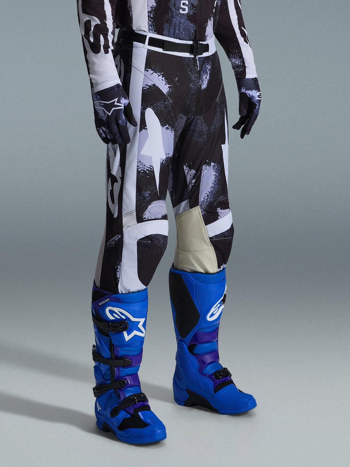 Alpinestars 2026 Racer Lahnd Pants, pantalones de motocross, patrón Iron Camo en gris y negro, usados con botas de carreras de color azul brillante y guantes a juego, con paneles blancos y rodillas interiores de cuero de cabra, equipamiento off-road de alto rendimiento
