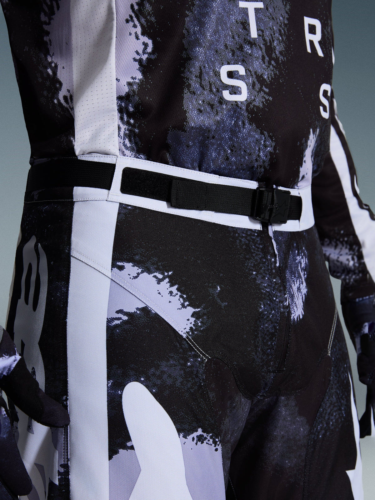 Pantalones Alpinestars Racer Lahnd 2026, pantalones de motocross en Iron Camo, vista de primer plano del cinturón ajustable y la hebilla magnética SX2, con un patrón de camuflaje gris y negro y construcción duradera en polietileno 600D.