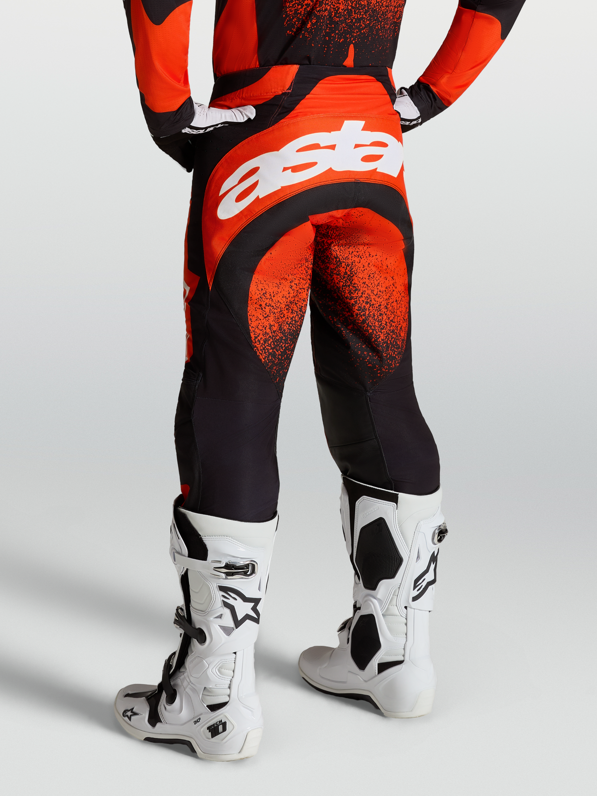Alpinestars Pantalones Techstar Swan, pantalones de motocross para hombre, rojos y negros, chasis elástico duradero con logo Astar blanco, mostrados en modelo con botas Tech 10 blancas