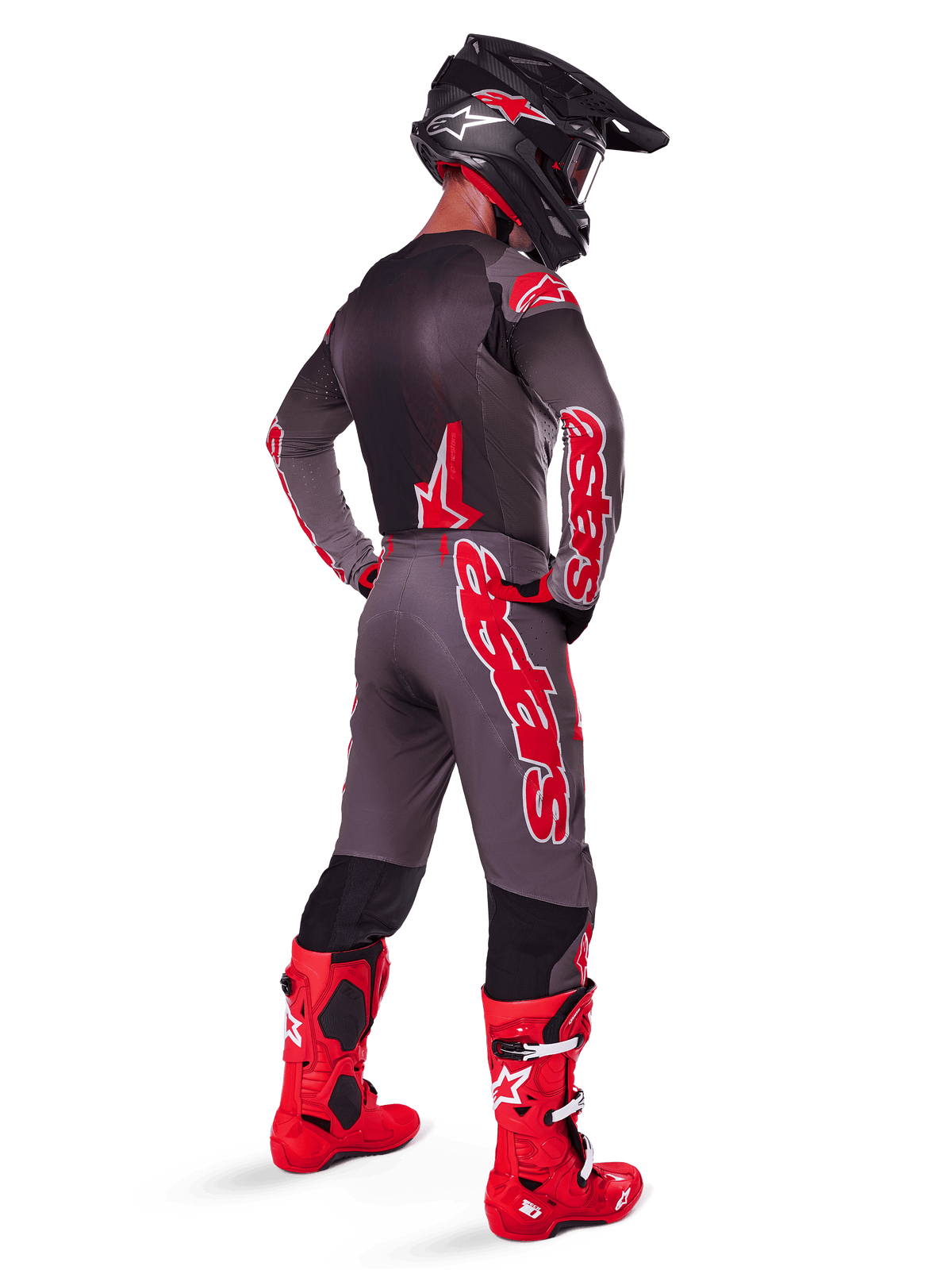 Piloto de motocross con pantalones Alpinestars 2025 Supertech Lipan, color Smoke Bright Red, pantalones grises con grandes logotipos rojos y paneles interiores negros, combinados con jersey gris a juego, casco negro y botas de color rojo brillante, equipamiento completo de carreras todoterreno visto desde atrás.