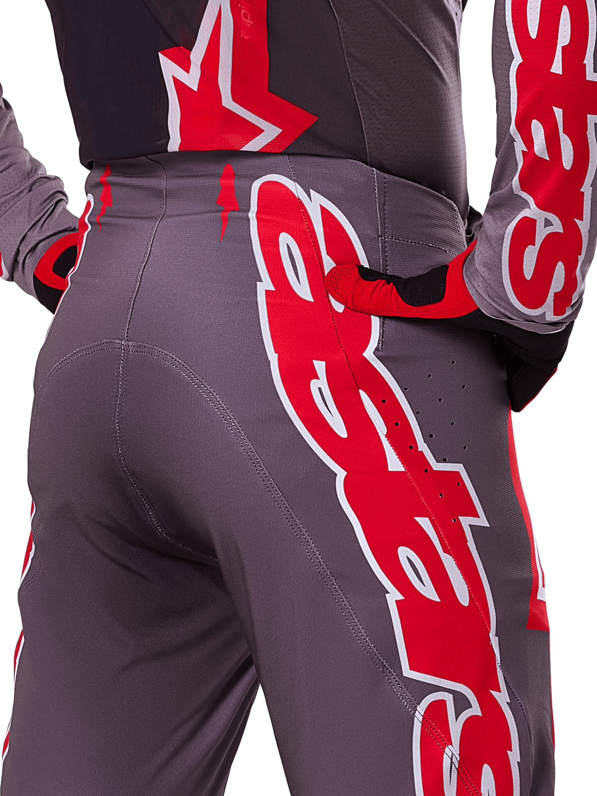 Alpinestars 2025 Supertech Lipan Pants, pantalones de motocross, Smoke Bright Red, vista de cerca posterior que muestra tejido gris oscuro con gráficos rojos llamativos, usados con guantes y jersey a juego en rojo y negro, con perforaciones de ventilación y costuras ergonómicas para rendimiento todoterreno