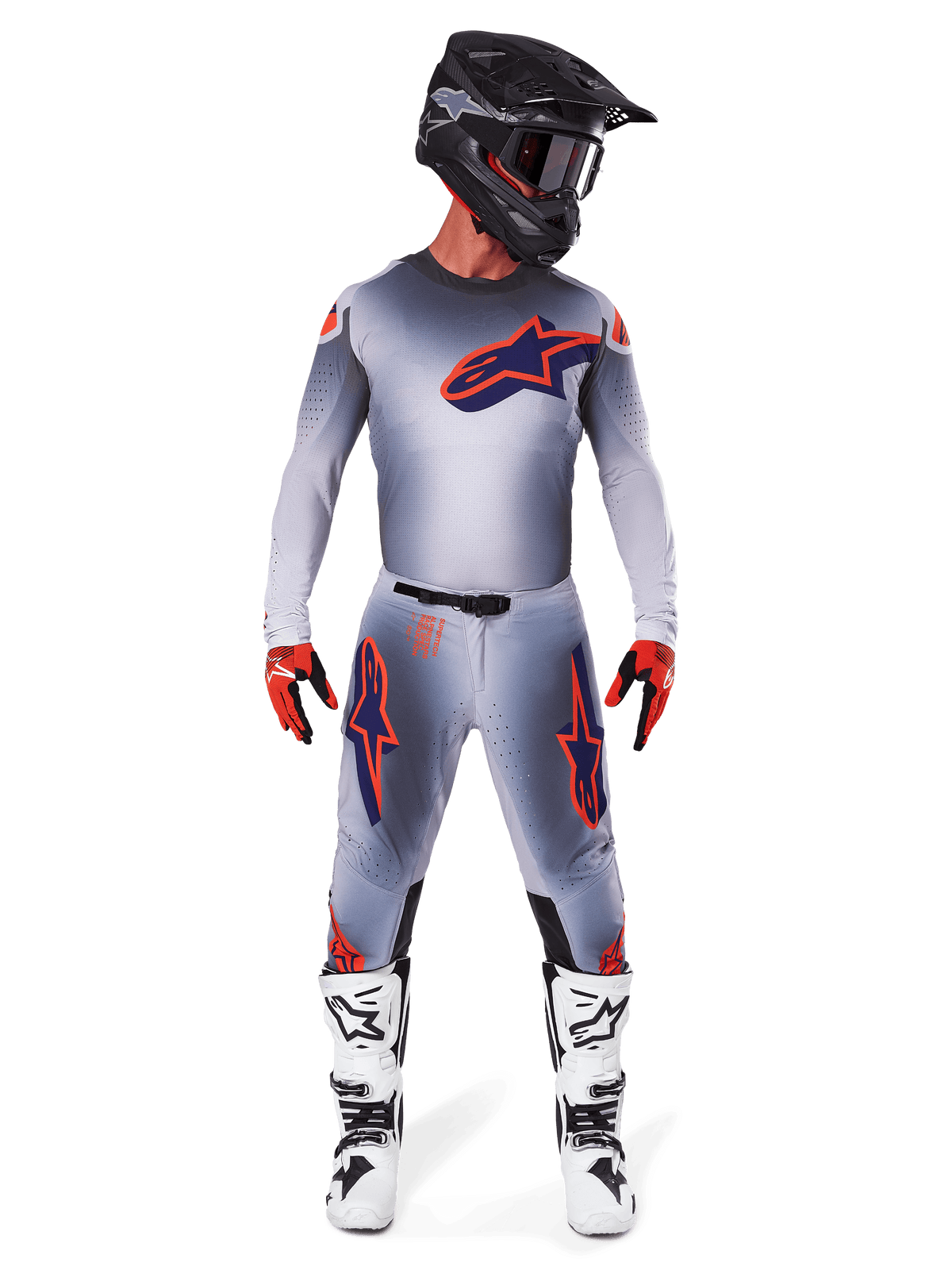 Piloto de motocross con pantalones Alpinestars Supertech Lipan 2025 y jersey a juego en Gris Naranja Flúor, con logotipos llamativos en naranja y azul marino, casco negro, guantes rojos y botas blancas y negras, kit de competición completo para rendimiento todoterreno.