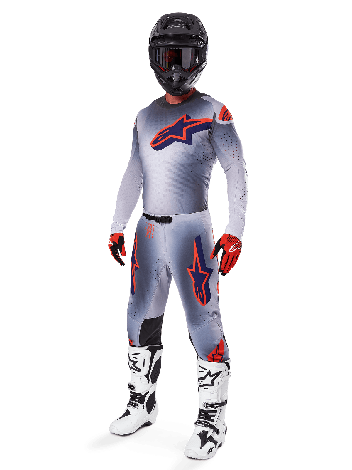 Piloto de motocross con el conjunto completo de equipamiento Alpinestars Supertech Lipan 2025, en gris y naranja flúor, jersey gris con logo naranja grande en el pecho, pantalones a juego con detalles naranjas, casco negro, guantes rojos y botas blancas, atuendo profesional de competición off-road