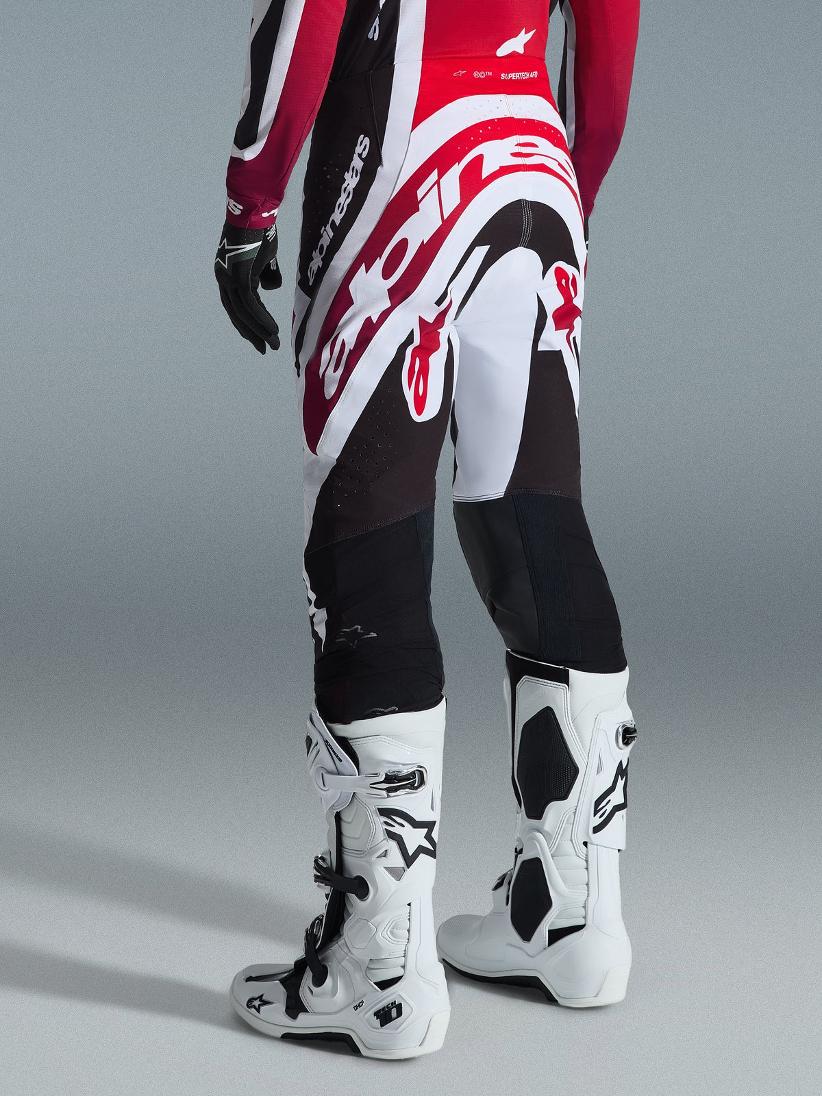 Pantalones Alpinestars Supertech AFD Vista 2026, pantalones de motocross, negro, rojo y blanco, vista trasera con gran logotipo de Alpinestars en el asiento, combinados con botas Tech 10 blancas y guantes negros, diseño atlético para un rendimiento de élite en off-road