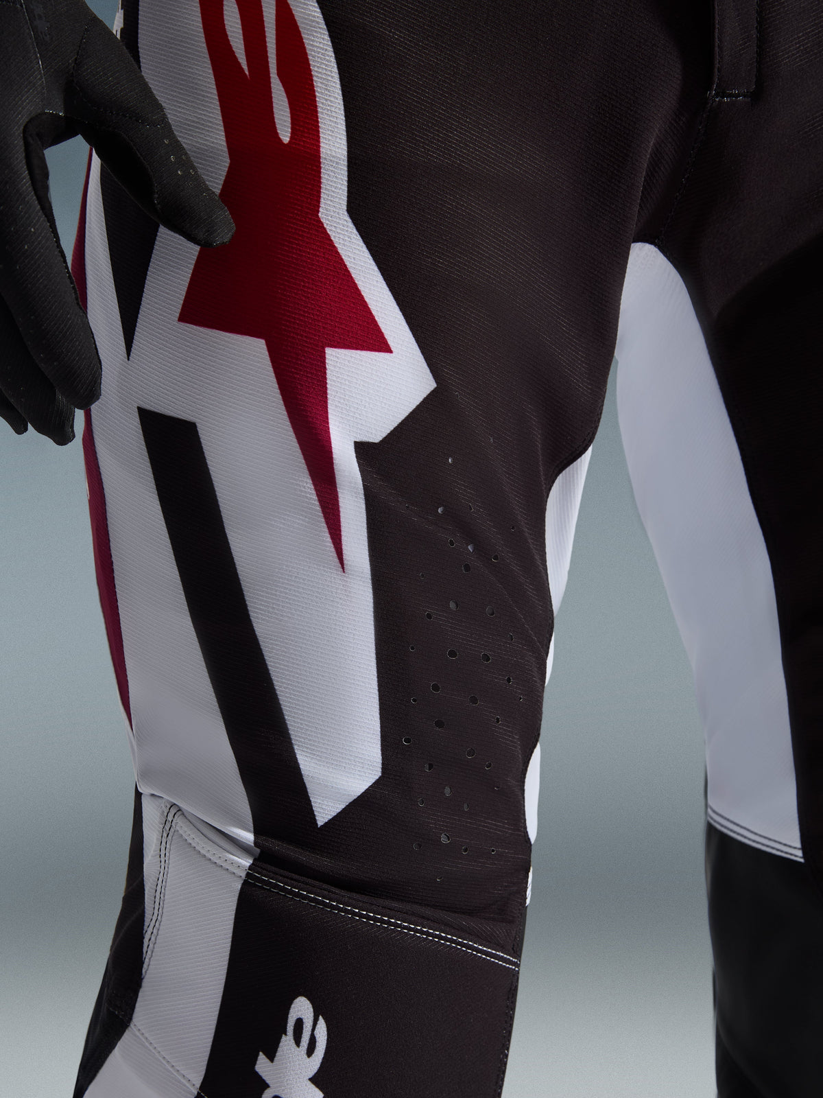 Alpinestars 2026 Supertech AFD Vista Pants, pantalones de motocross, negro, rojo y blanco, primer plano de la zona del muslo con un gran logotipo de estrella en rojo y blanco, perforaciones cortadas con láser para el flujo de aire y tejido ripstop elástico duradero.