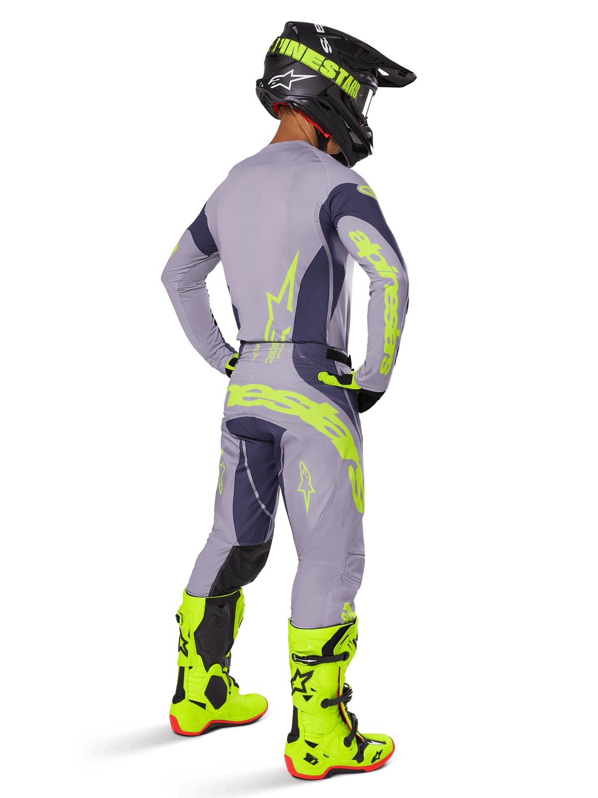 Piloto de motocross visto desde atrás vistiendo equipamiento completo de competición, incluyendo los pantalones Alpinestars Techstar Dreem 2025 en gris y gris oscuro con llamativos acentos en amarillo neón, jersey gris a juego con gráficos neón, botas amarillo neón brillante y casco negro, conjunto profesional de motocross coordinado