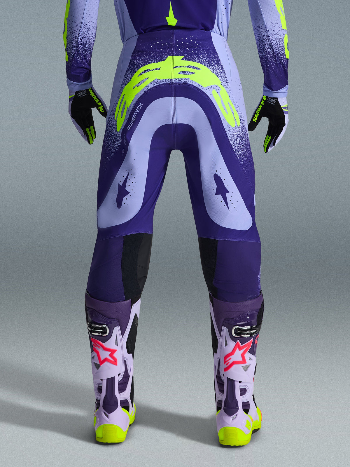 Alpinestars 2026 Supertech Scenz Pants, Motocross Pants, Purple and Yellow Fluo, rear view showing large yellow logo on seat, worn with matching jersey, gloves, and protective boots, athletic fit for professional motocross racing.