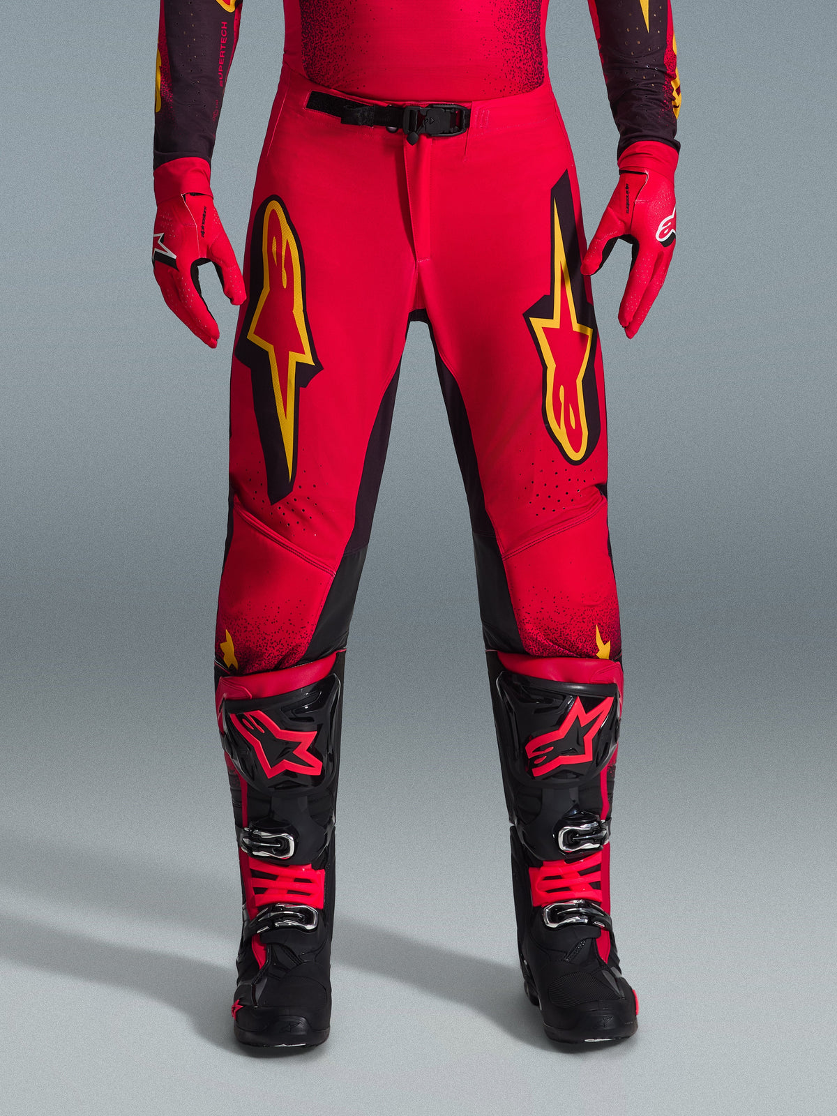 Alpinestars Pantalones Supertech Scenz 2026, pantalones de motocross, rojos, negros y amarillos, ajuste atlético de nivel profesional con grandes logotipos de estrellas amarillas en los muslos, combinados con guantes rojos a juego y botas técnicas negras y rojas, diseñados para un rendimiento de élite en carreras todoterreno