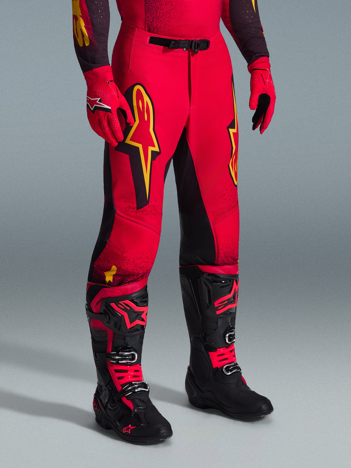 Alpinestars 2026 Supertech Scenz Pants, pantalones de motocross, rojos, negros y amarillos, con logotipos de Alpinestars en amarillo y paneles negros, combinados con jersey rojo a juego, guantes rojos y botas de motocross negras.
