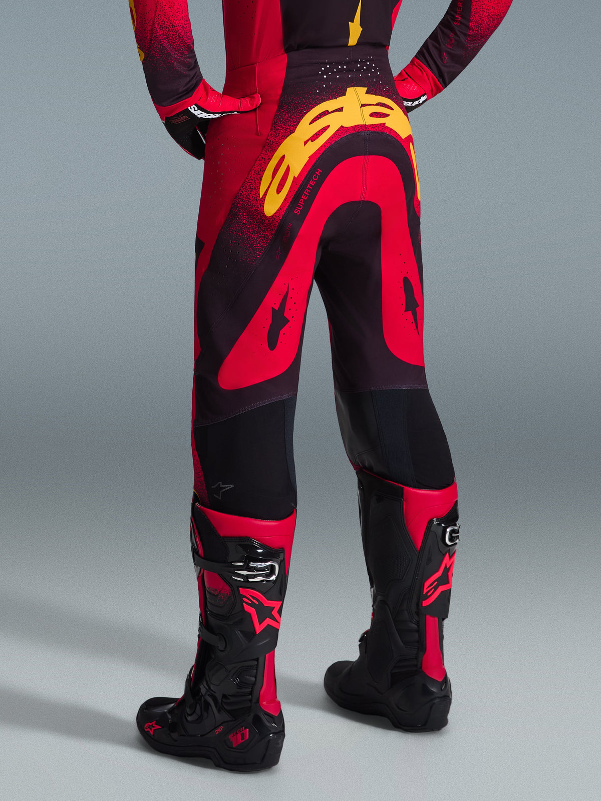 Alpinestars Supertech Scenz Pants 2026, pantalones de motocross, rojo, negro y amarillo, vista posterior que muestra el gran logotipo amarillo de Alpinestars en la zona del asiento, usados con un jersey a juego y botas de motocross rojas y negras