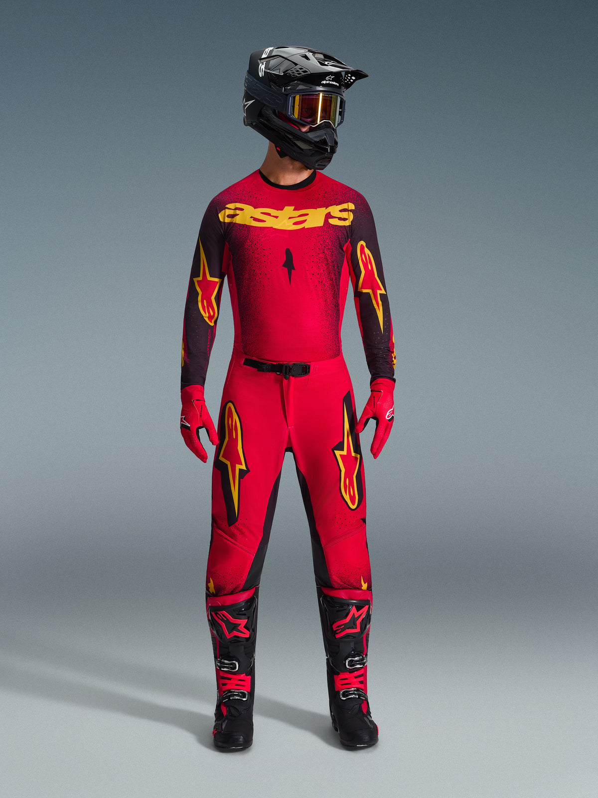 Pantalones Alpinestars 2026 Supertech Scenz, pantalones de motocross en rojo, negro y amarillo, usados por un piloto en un conjunto completo de equipamiento de competición, jersey a juego rojo y negro con logos amarillos, casco negro, guantes rojos y botas negras, diseño atlético pro-fit para competición off-road