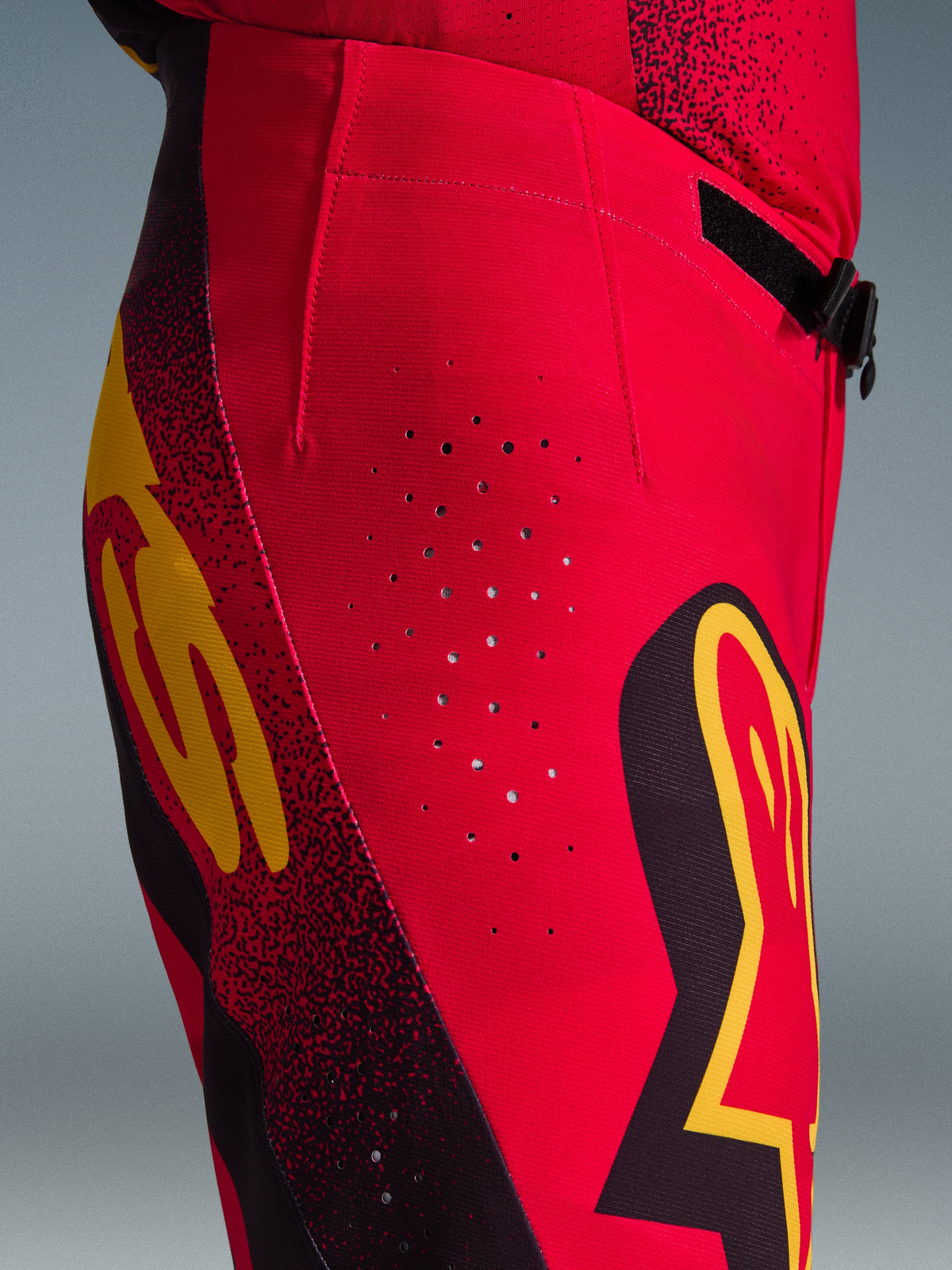 Pantalones Alpinestars Supertech Scenz 2026, pantalones de motocross, rojo, negro y amarillo, vista lateral en primer plano con perforaciones de ventilación cortadas con láser, logotipos gráficos llamativos y tejido rip-stop elástico de alto rendimiento para carreras de motocross.