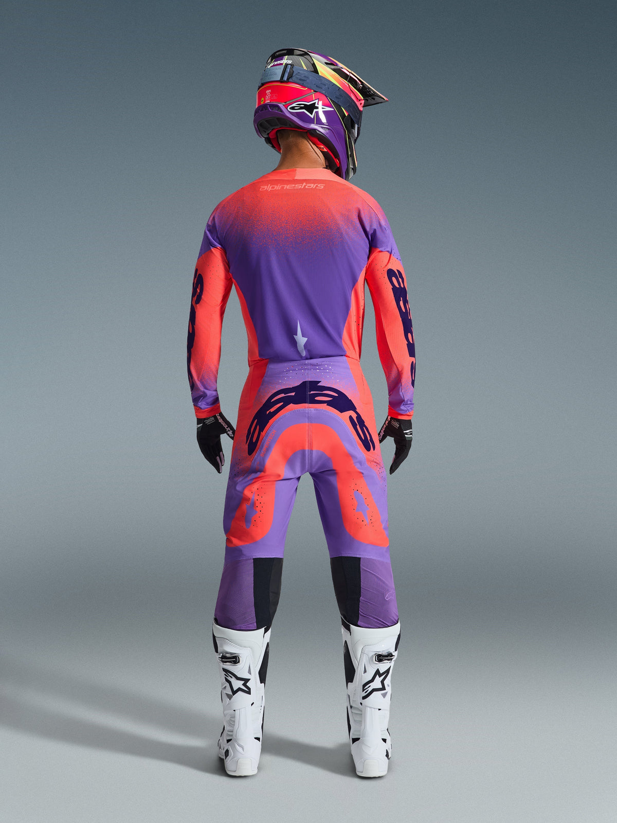 Alpinestars 2026 Supertech Scenz Pants, Motocross Pants, Hot Coral and Purple, rear view of motocross rider wearing a complete racing gear set, featuring vibrant gradient design with bold rear logos, paired with a matching jersey, helmet, and white boots.