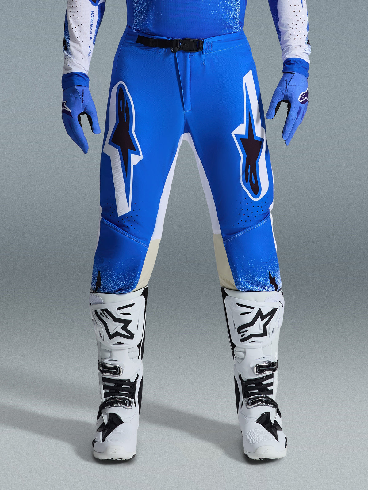 Alpinestars 2026 Supertech Scenz Pants, pantalones de motocross, azul UCLA y blanco, usados con guantes azules a juego y botas blancas, con grandes gráficos blancos y negros en los muslos, ajuste atlético para rendimiento todoterreno