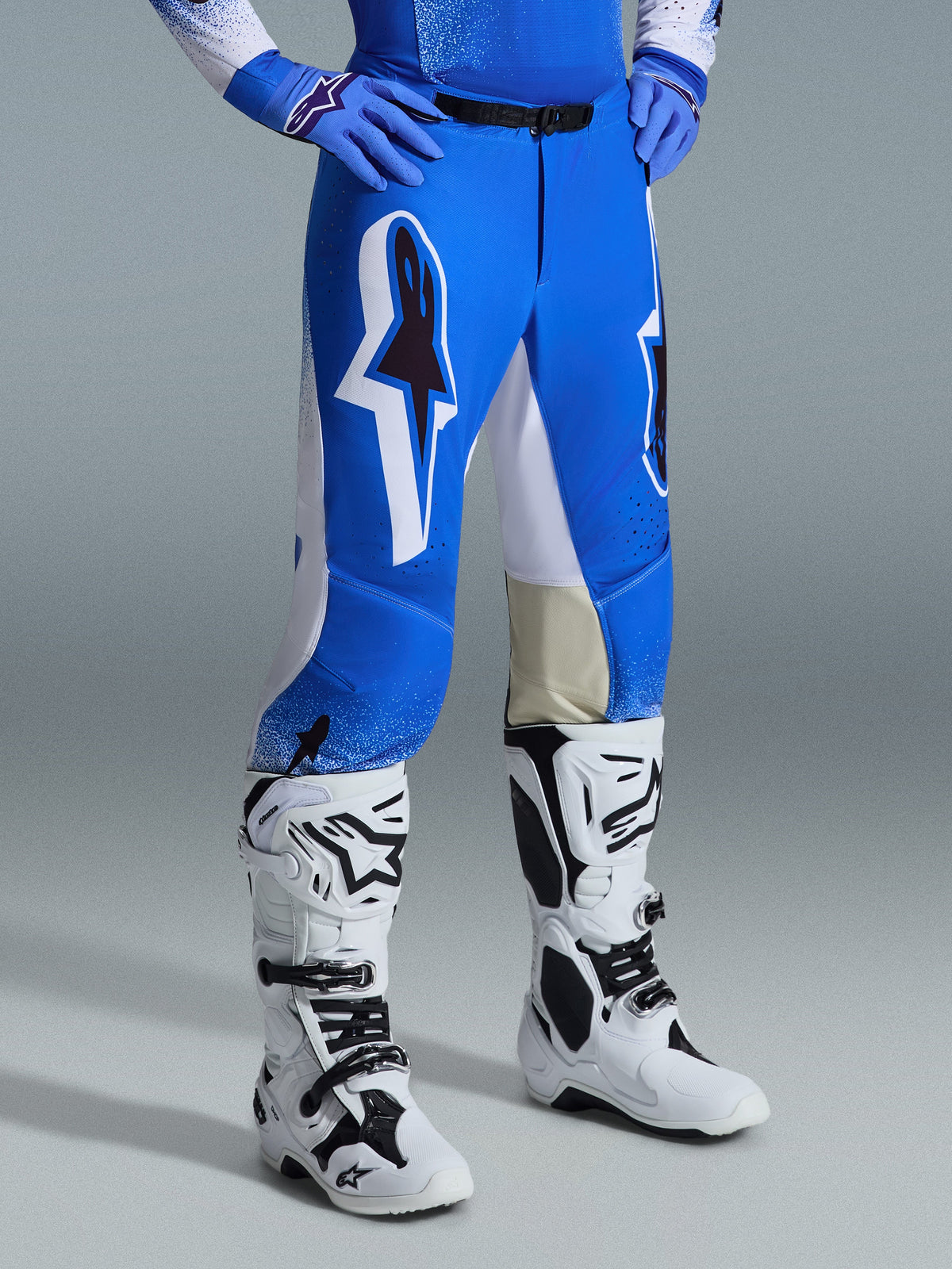 Alpinestars Supertech Scenz Pants 2026, pantalones de motocross, azul Ucla y blanco, usados con botas blancas y negras y guantes azules, con grandes logotipos gráficos en los muslos y paneles blancos, ajuste atlético diseñado para motocross competitivo