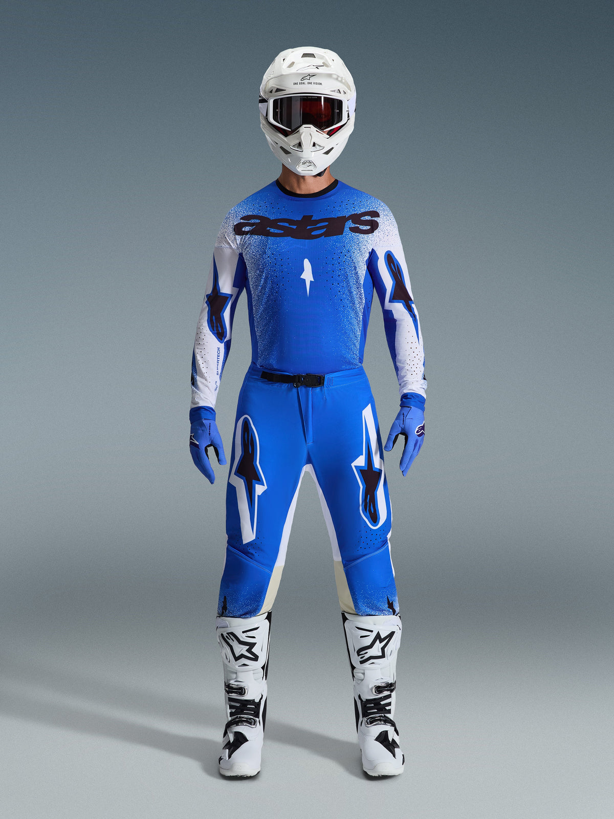 Piloto de motocross con equipamiento completo de competición, jersey azul y blanco con marca astars en negro, pantalones Supertech Scenz 2026 en Ucla Blue White con logotipos de estrellas destacados, casco blanco, guantes azules y botas blancas, conjunto deportivo coordinado