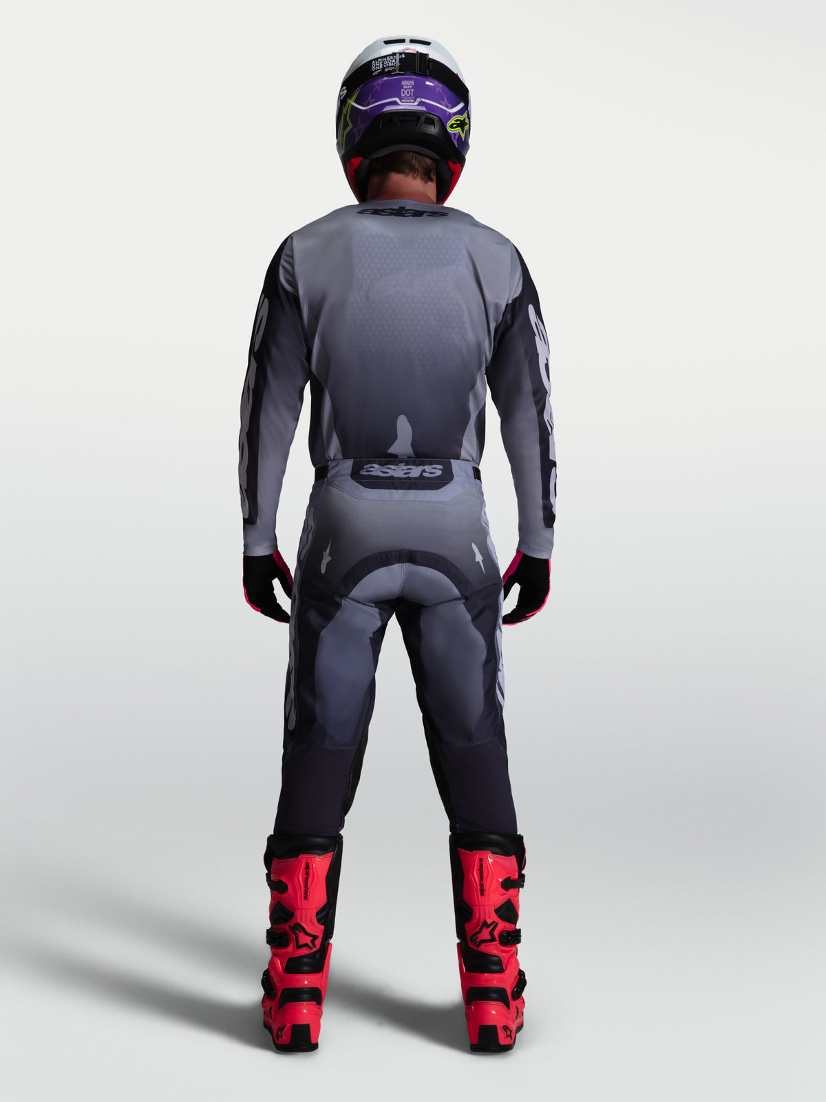 Pantalones Racer Amber de Alpinestars, conjunto de motocross para hombre en gris y lila, vista posterior con botas rojas.
