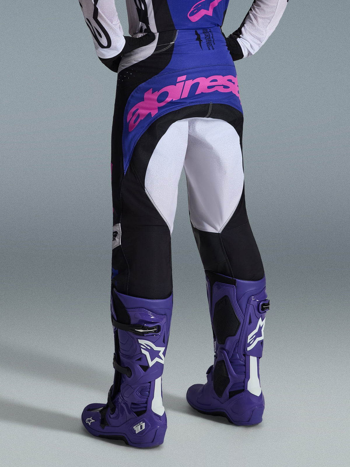 Alpinestars 2026 Techstar Knif Pants, pantalones de motocross, negro, gris claro y púrpura, vista trasera con logotipo rosa en el asiento, usados con jersey a juego y botas de motocross púrpuras, traje profesional de competición off-road